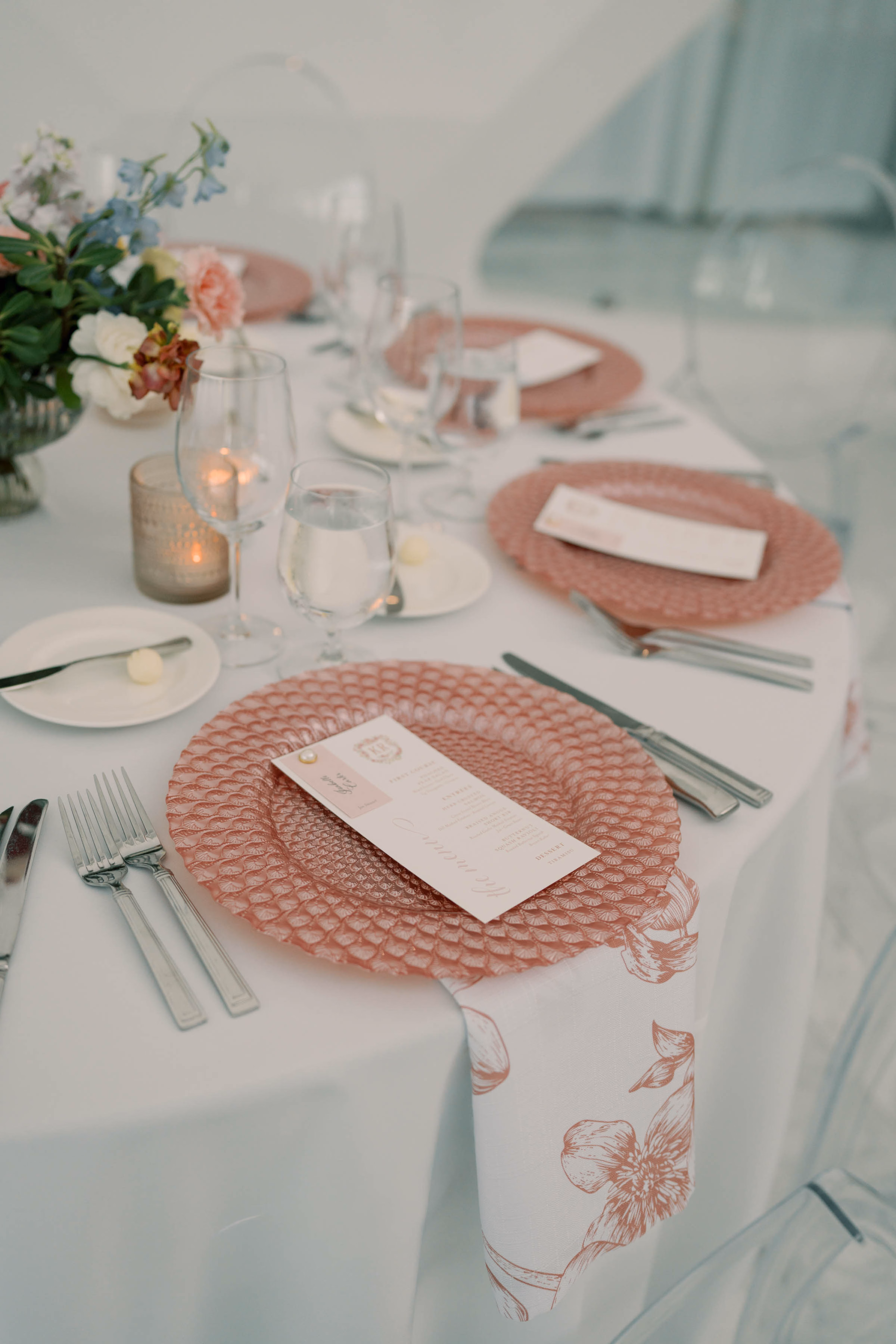 Modern luxury wedding tablescape rentals in Milwaukee, WI, by Tablescapes Event Rentals, featuring textured pink glass charger plates, floral print napkins, white table linens, elegant silverware, and clear acrylic ghost chairs.