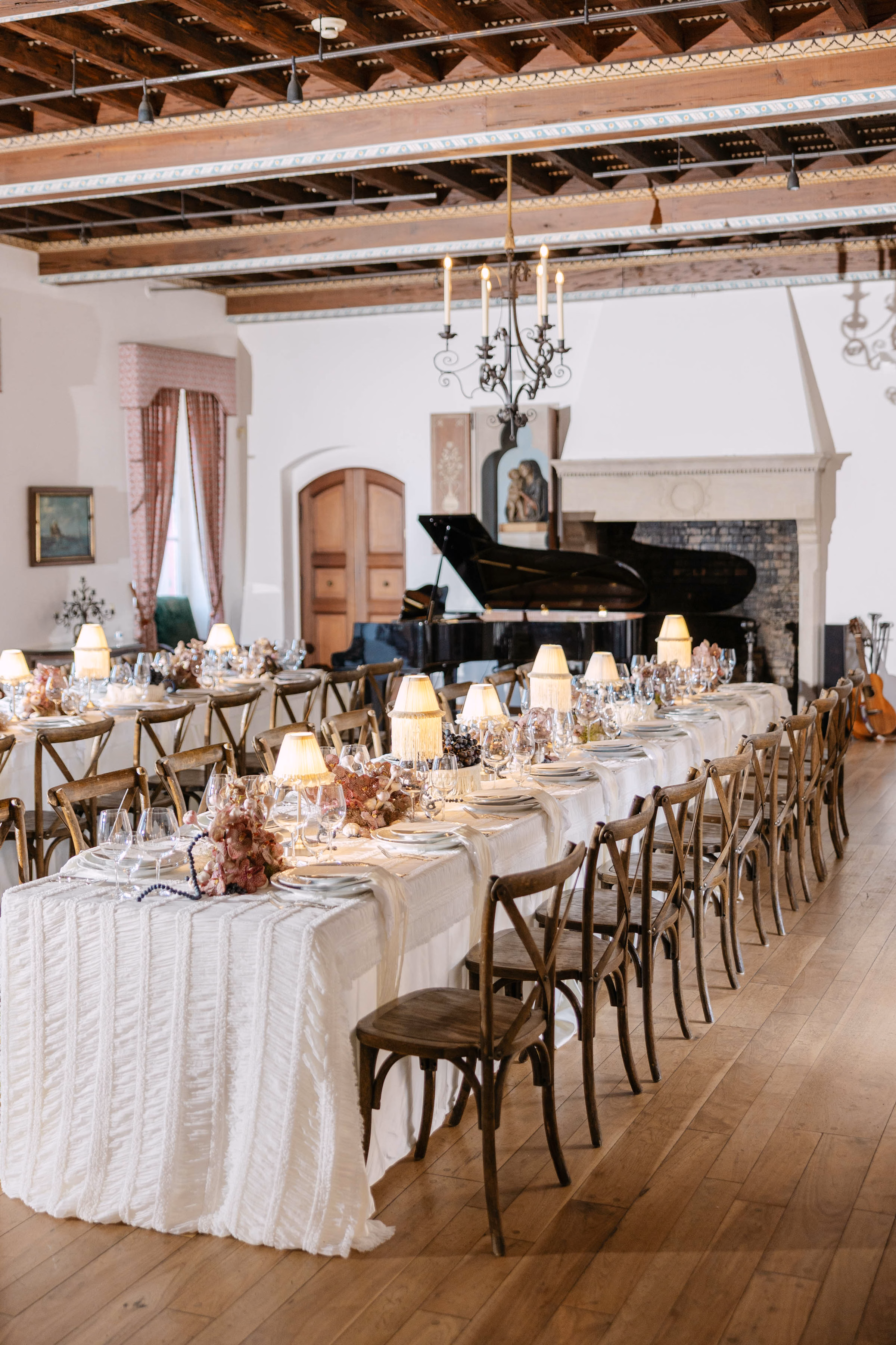 Luxury wedding reception tablescape rentals in Milwaukee, WI, by Tablescapes Event Rentals, featuring long banquet tables with textured white linens, wooden cross-back chairs, fine dining stemware, and small fringed table lamps.