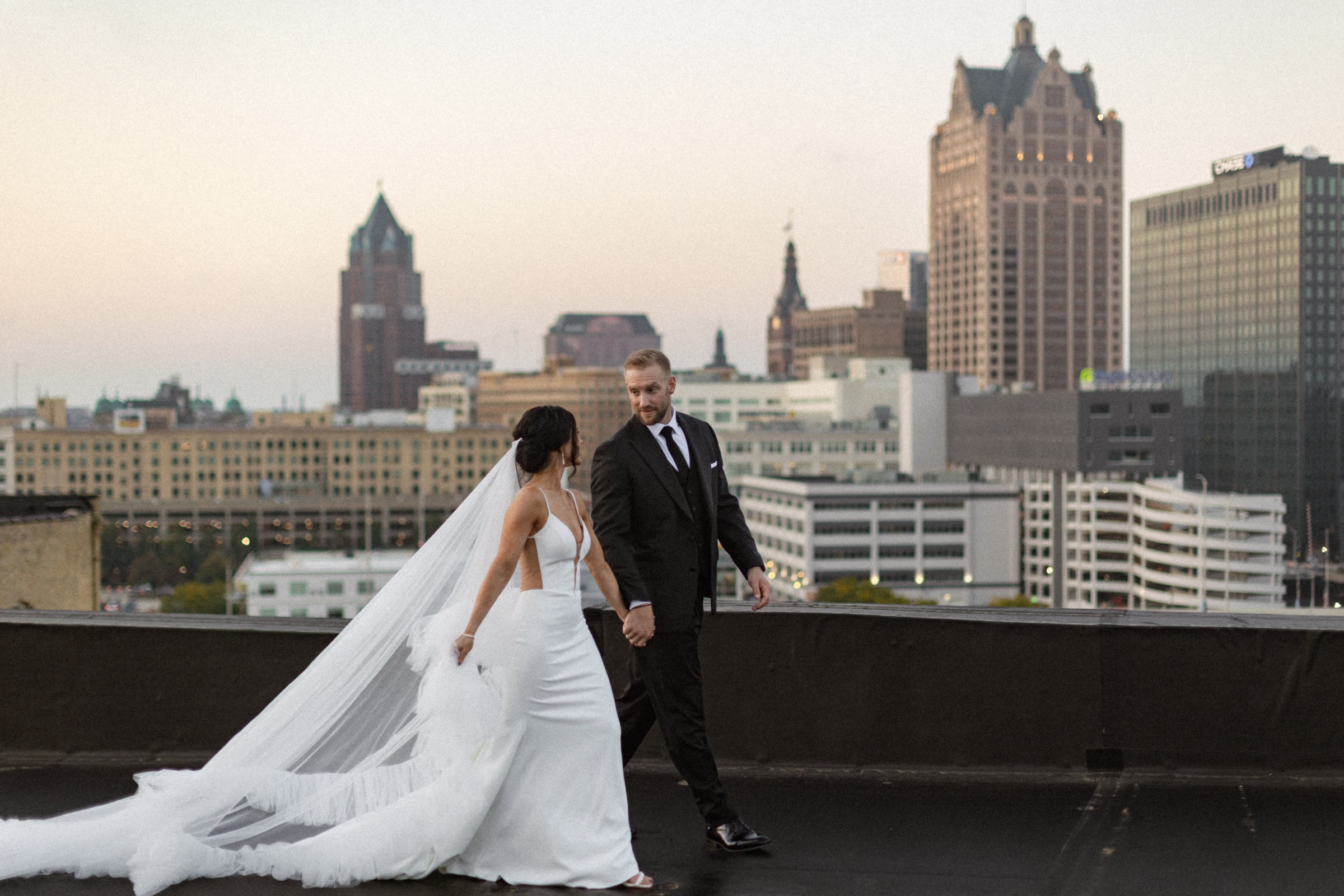 a rooftop portrait of the couple walking side-by-side, with city views of Milwaukee behind them
