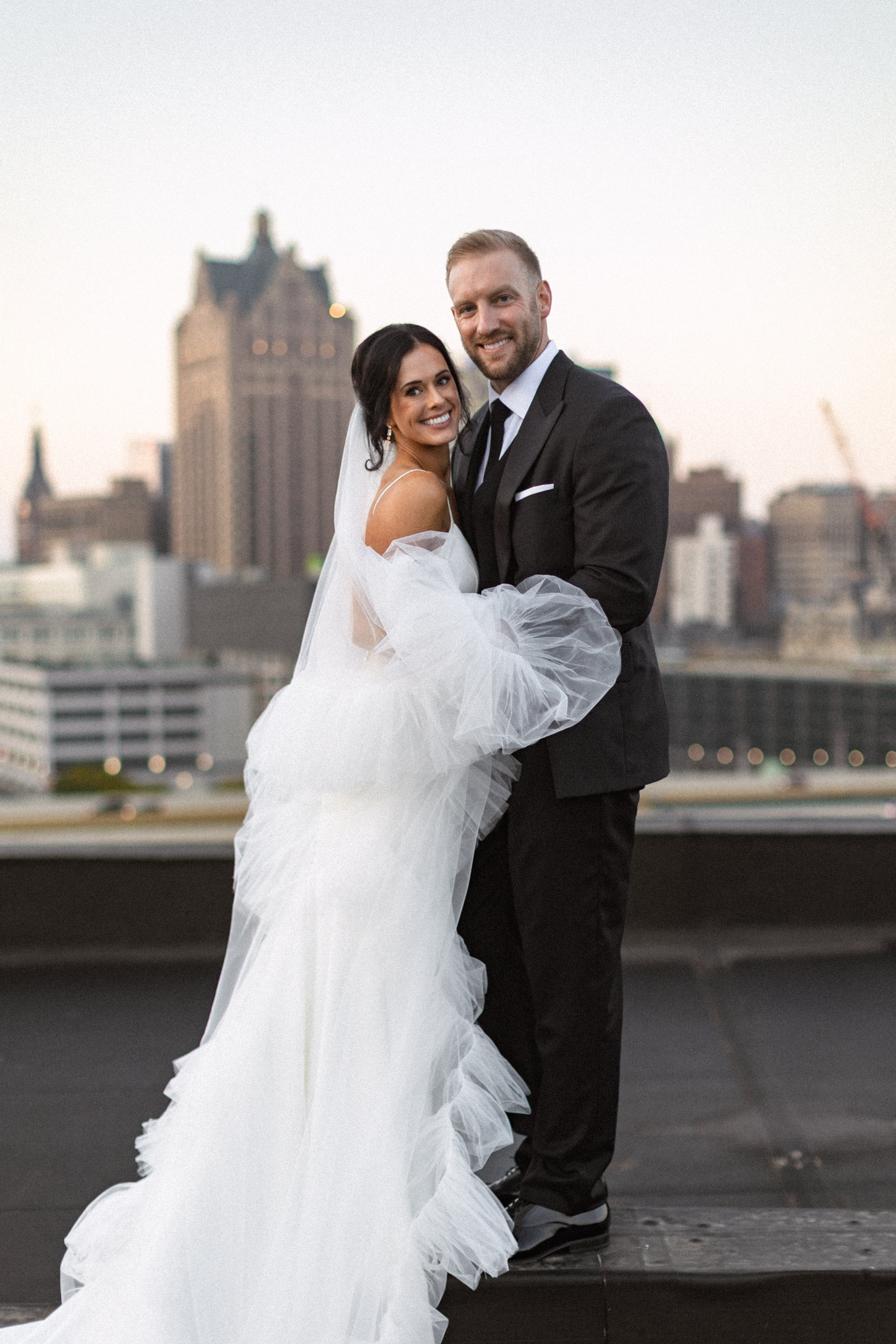 a newlywed couple smiles, set against the Milwaukee skyline at sunset