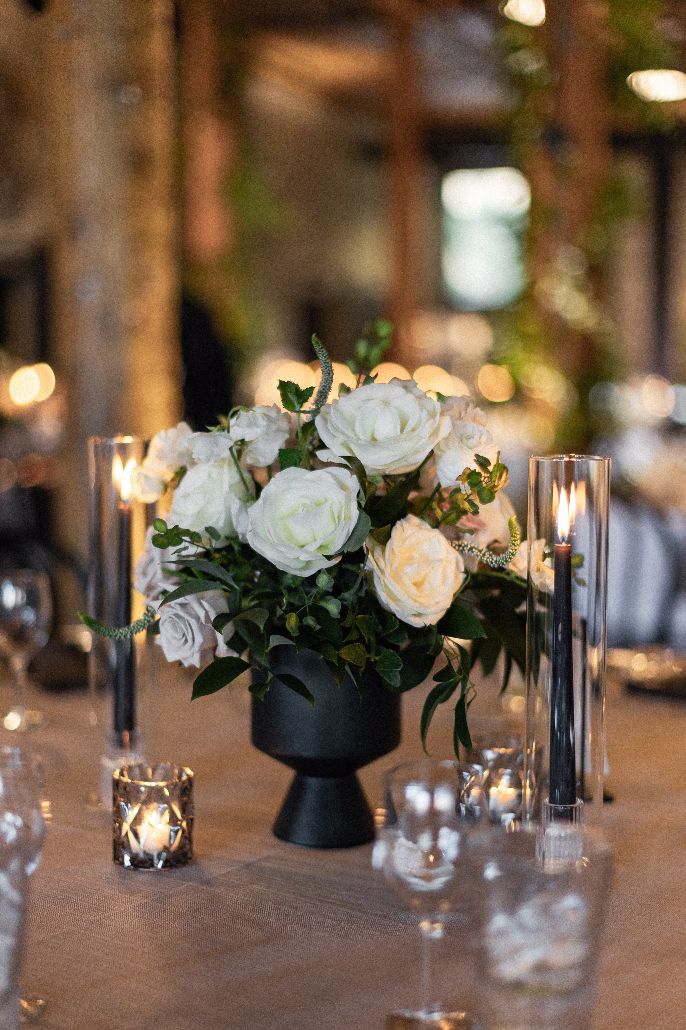 a floral centerpiece of roses sits beside lit candles