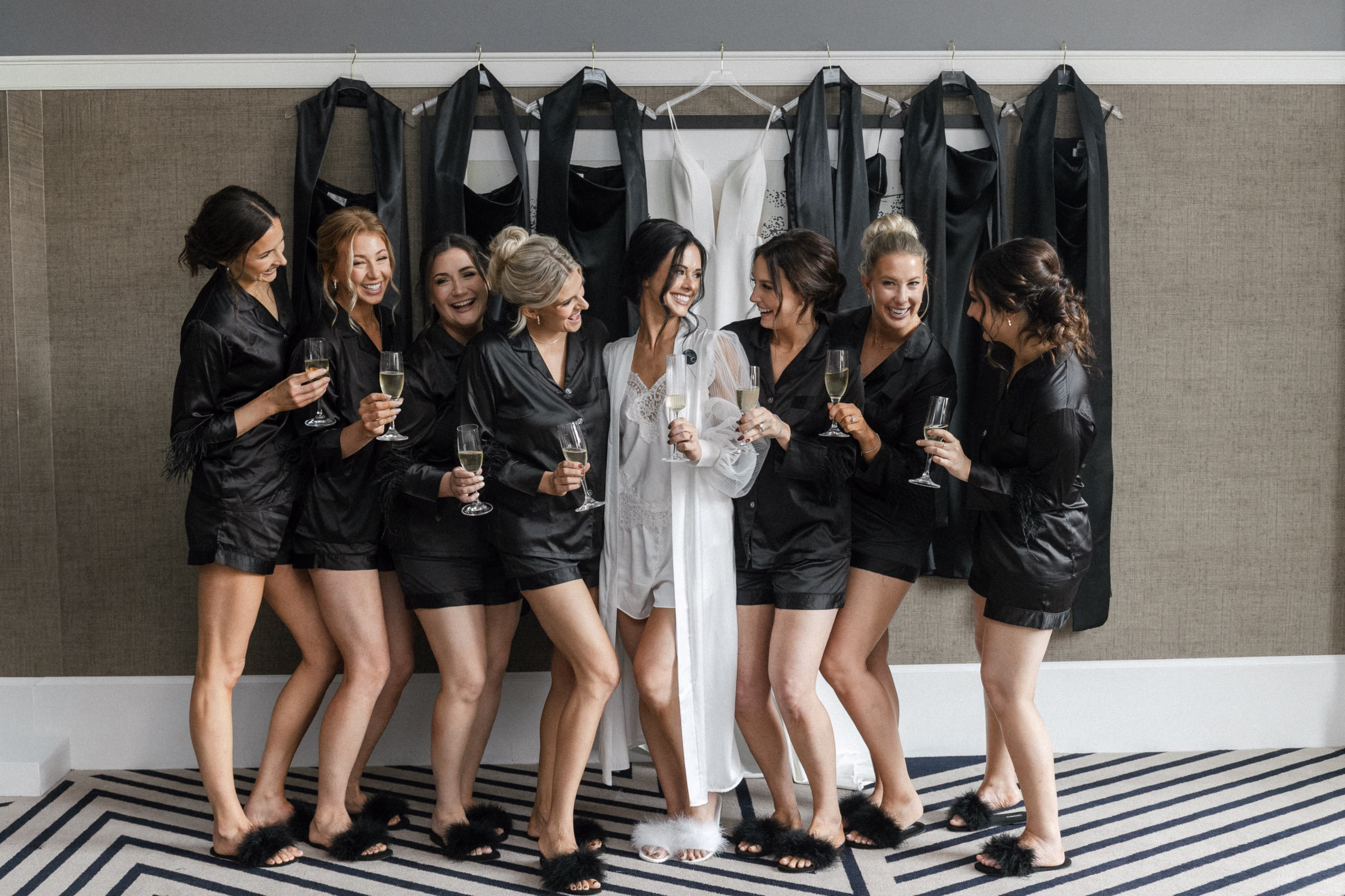 the bride and bridal party hold champagne dresses while in matching pajamas, preparing for the wedding day