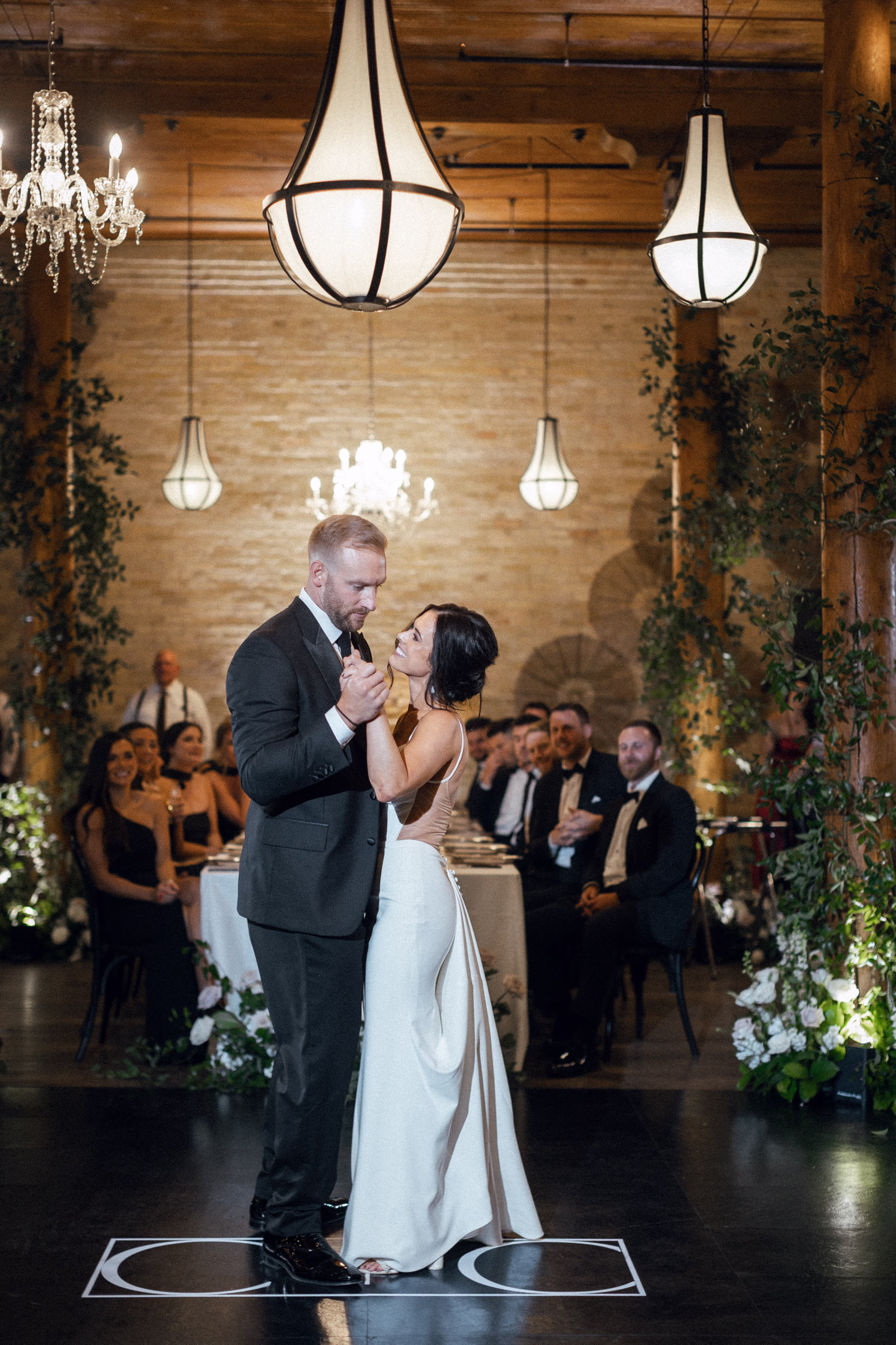 the couple shares a first dance at Pritzlaff Events in Milwaukee, Wisconsin, surrounded by florals, crawling vines, and chandeliers