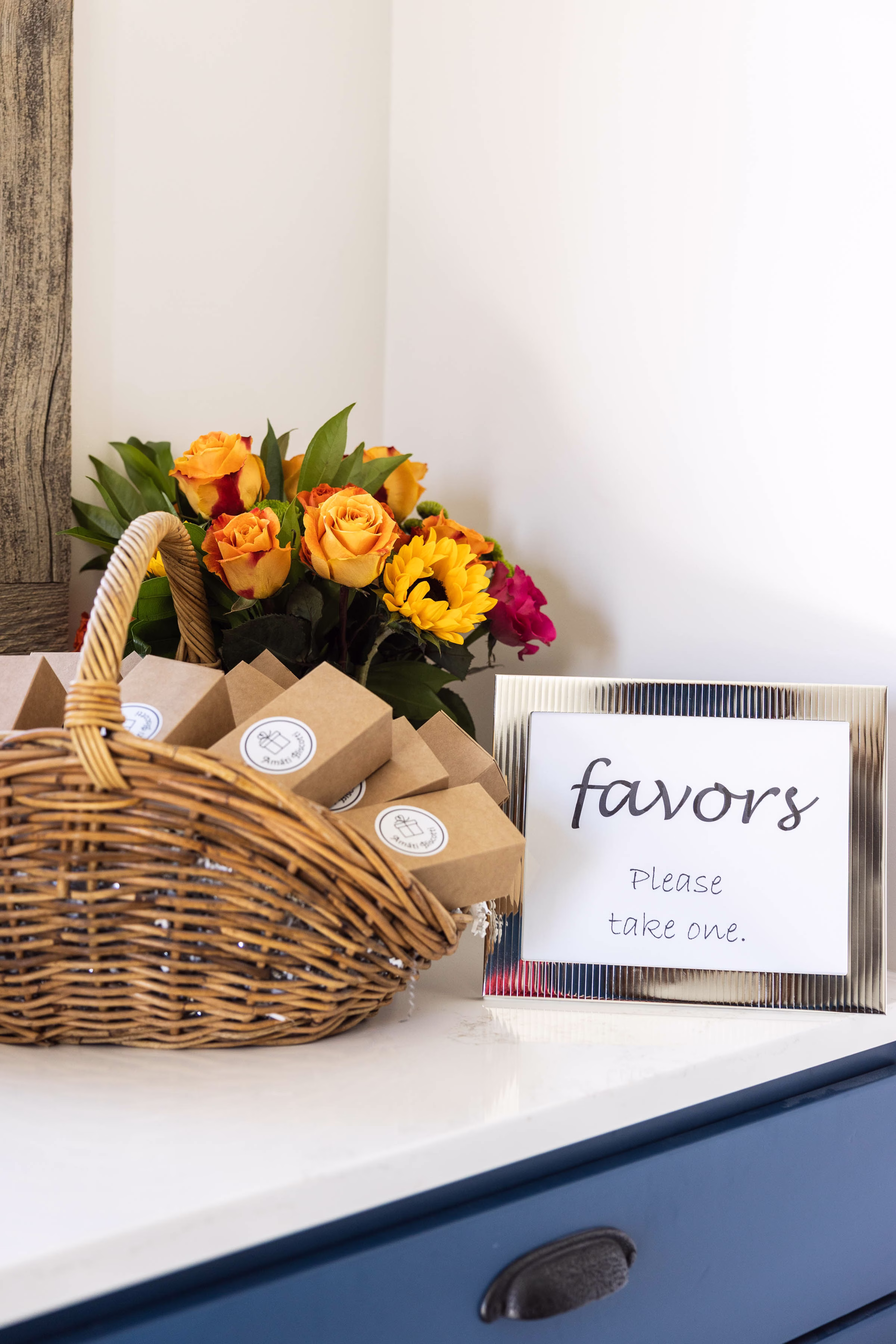 Amati Biscotti wedding favor boxes in a basket with sunflowers and roses beside a "favors, please take one" sign