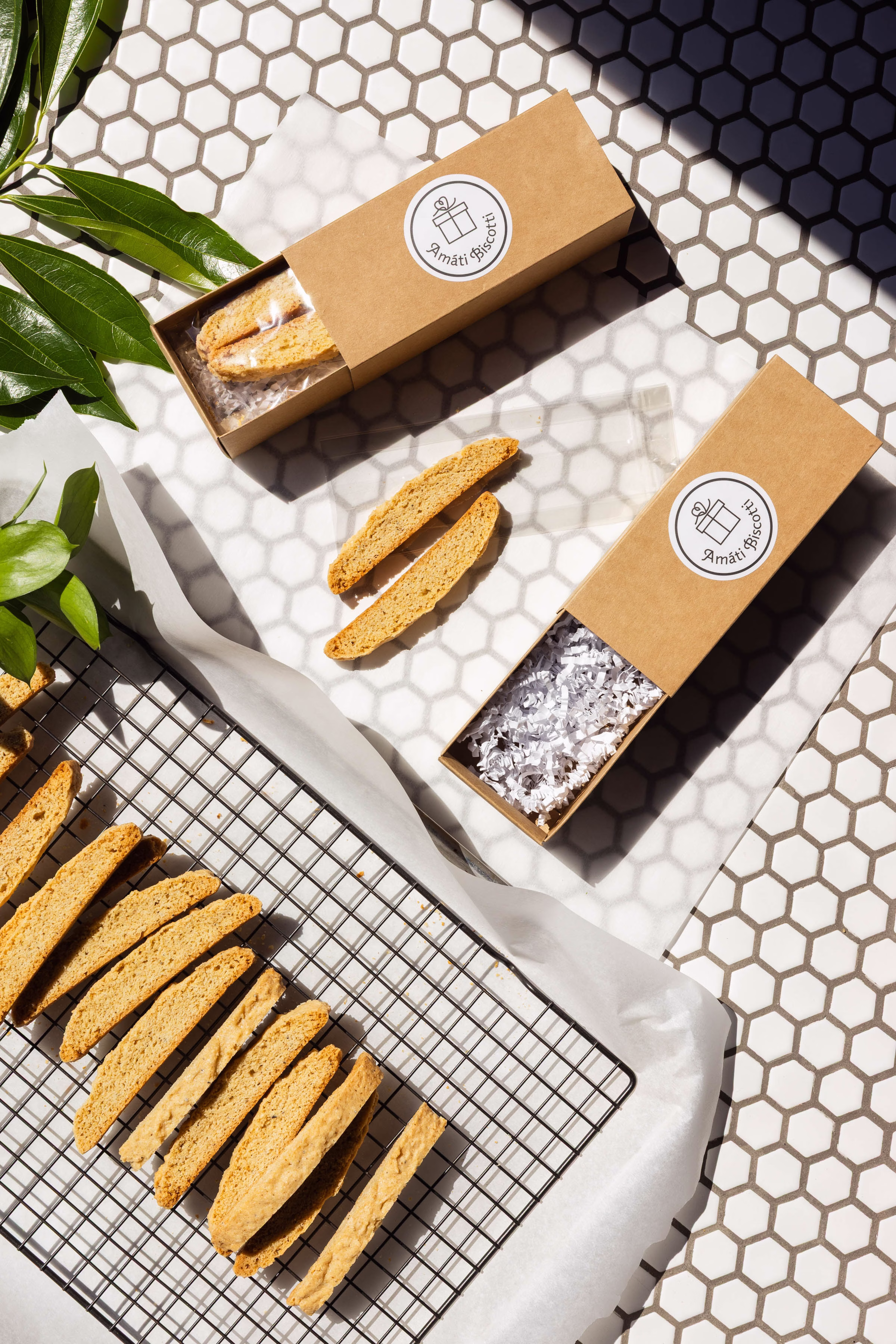 Amati Biscotti gift boxes being packaged with sliced biscotti cooling on a rack nearby