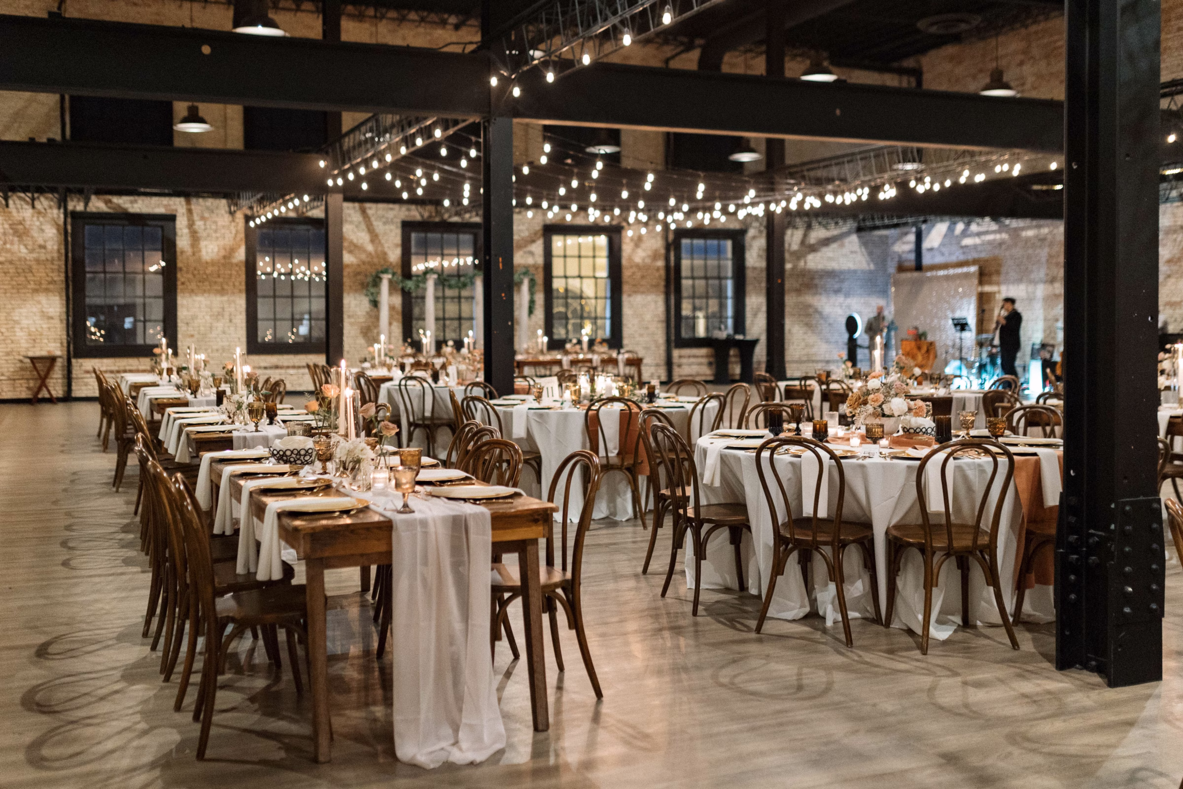 The Berkshire wedding reception space set with long and round tables, string lights, and exposed brick in Sheboygan, WI