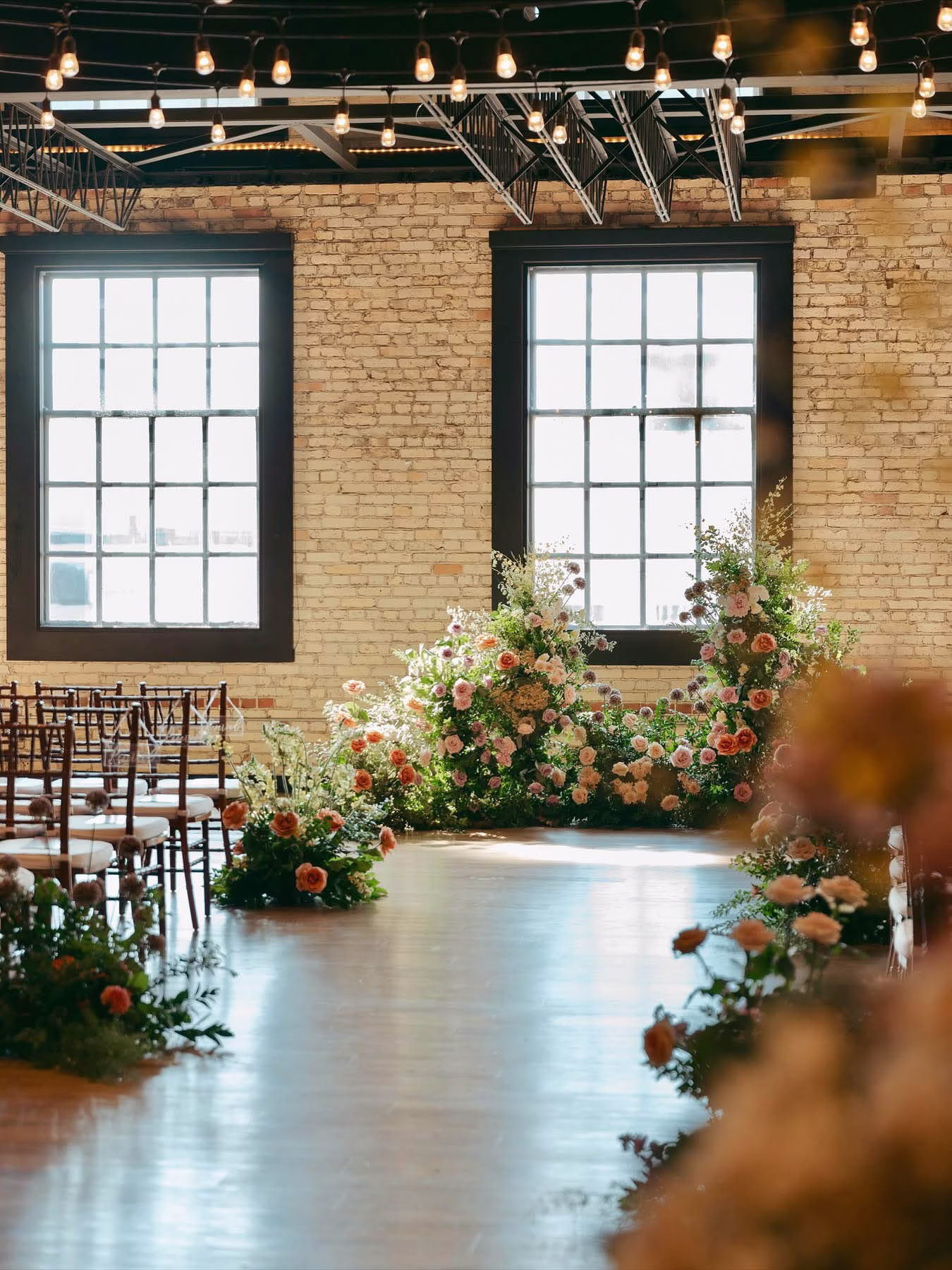 The Berkshire ceremony space with pink and white floral arch against exposed cream city brick and string lights