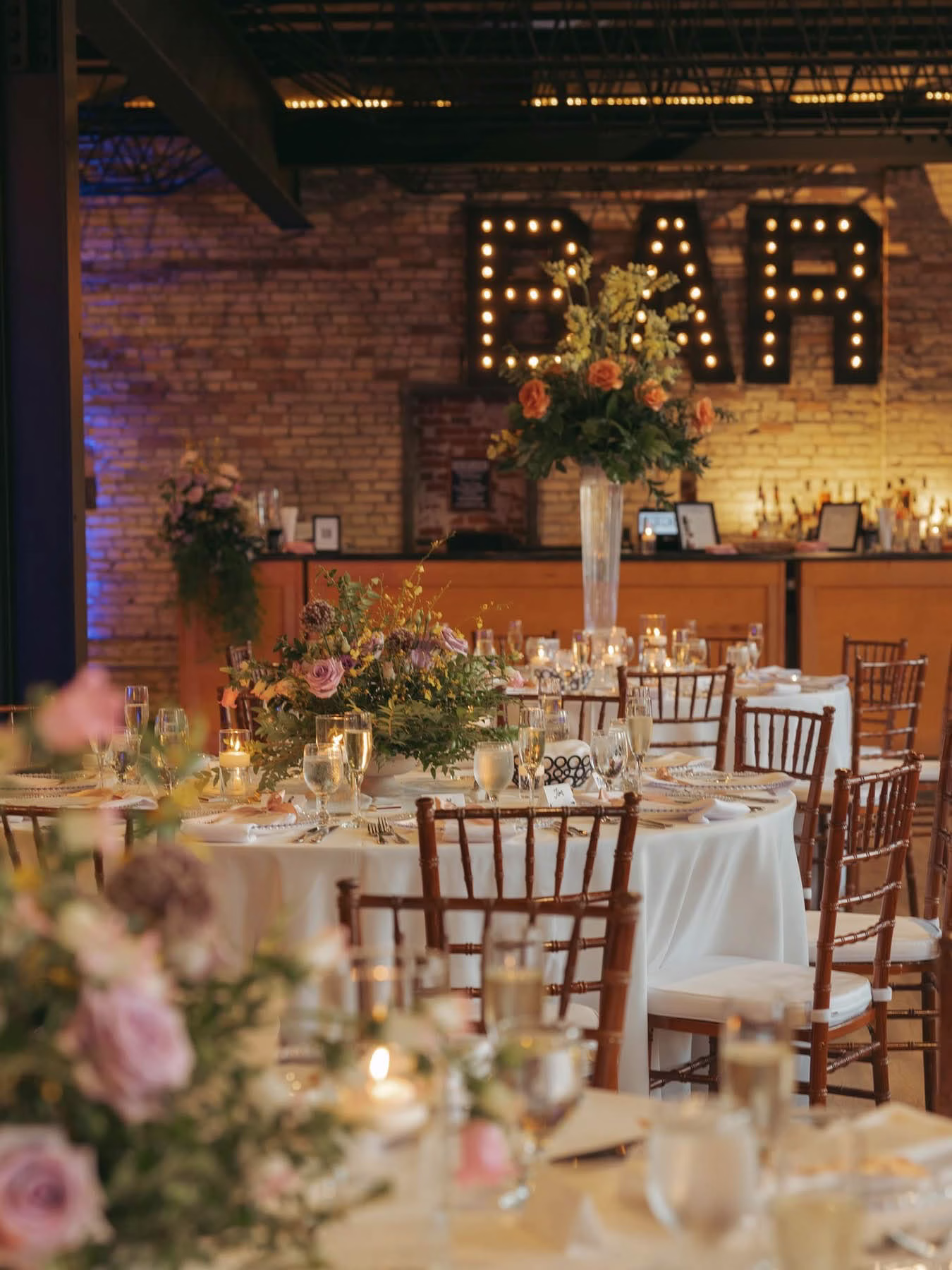 The Berkshire reception tables set with florals and candlelight in front of the venue's lit-up "BAR" sign