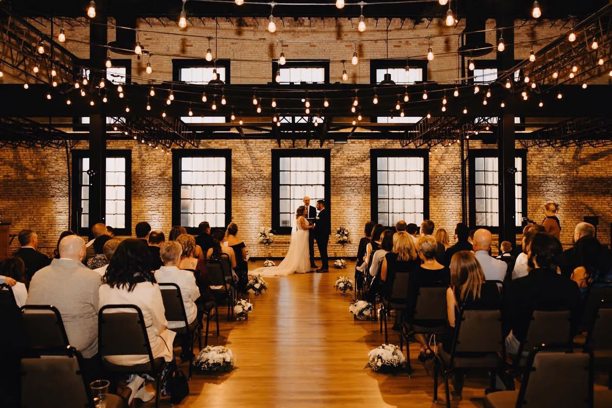 The Berkshire wedding ceremony with guests seated under string lights and exposed brick walls in Sheboygan