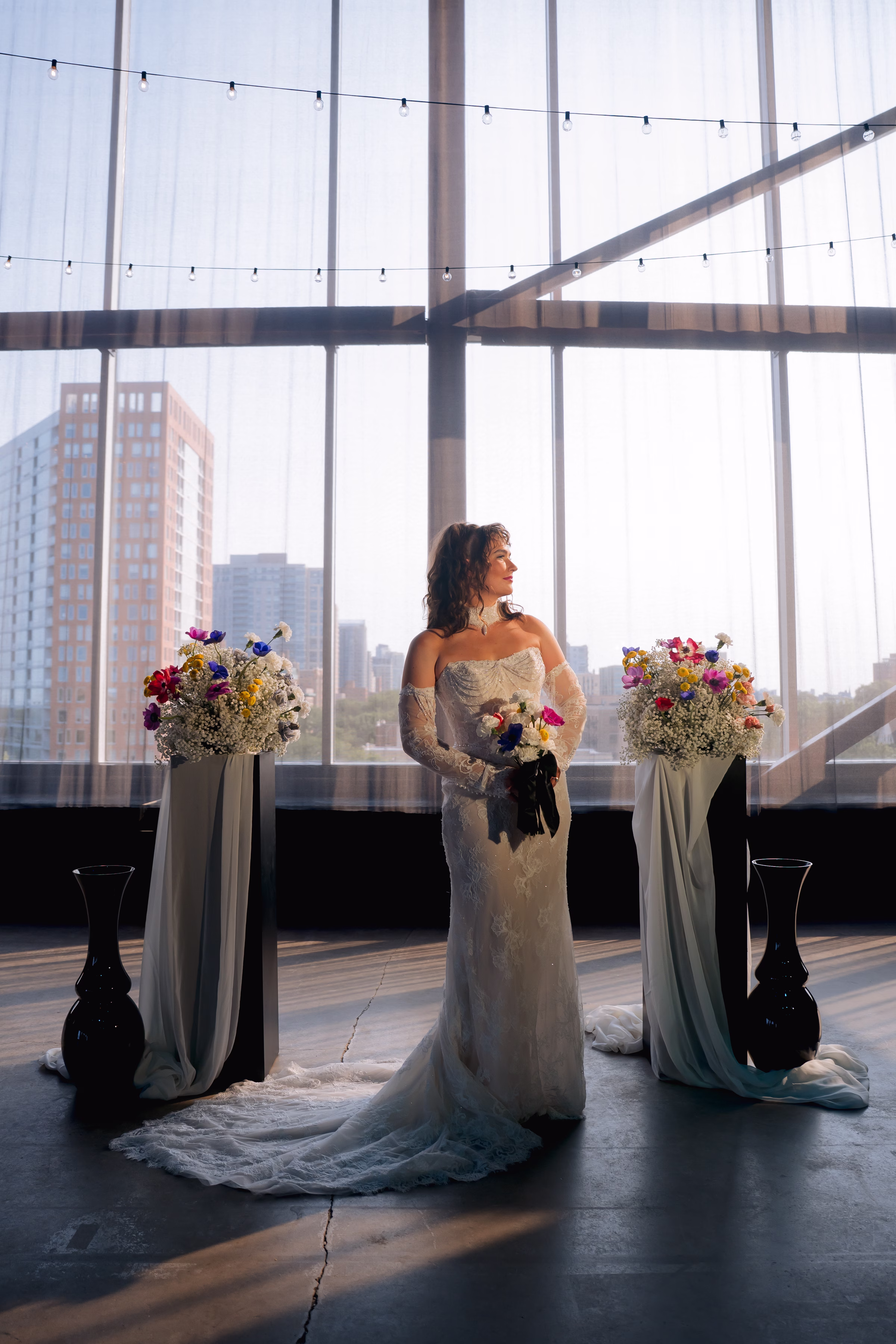 model Maggie poses in front of the ceremony scene at Jan Serr Studio framed by florals, décor, sunshine, and a view of the Milwaukee skyline
