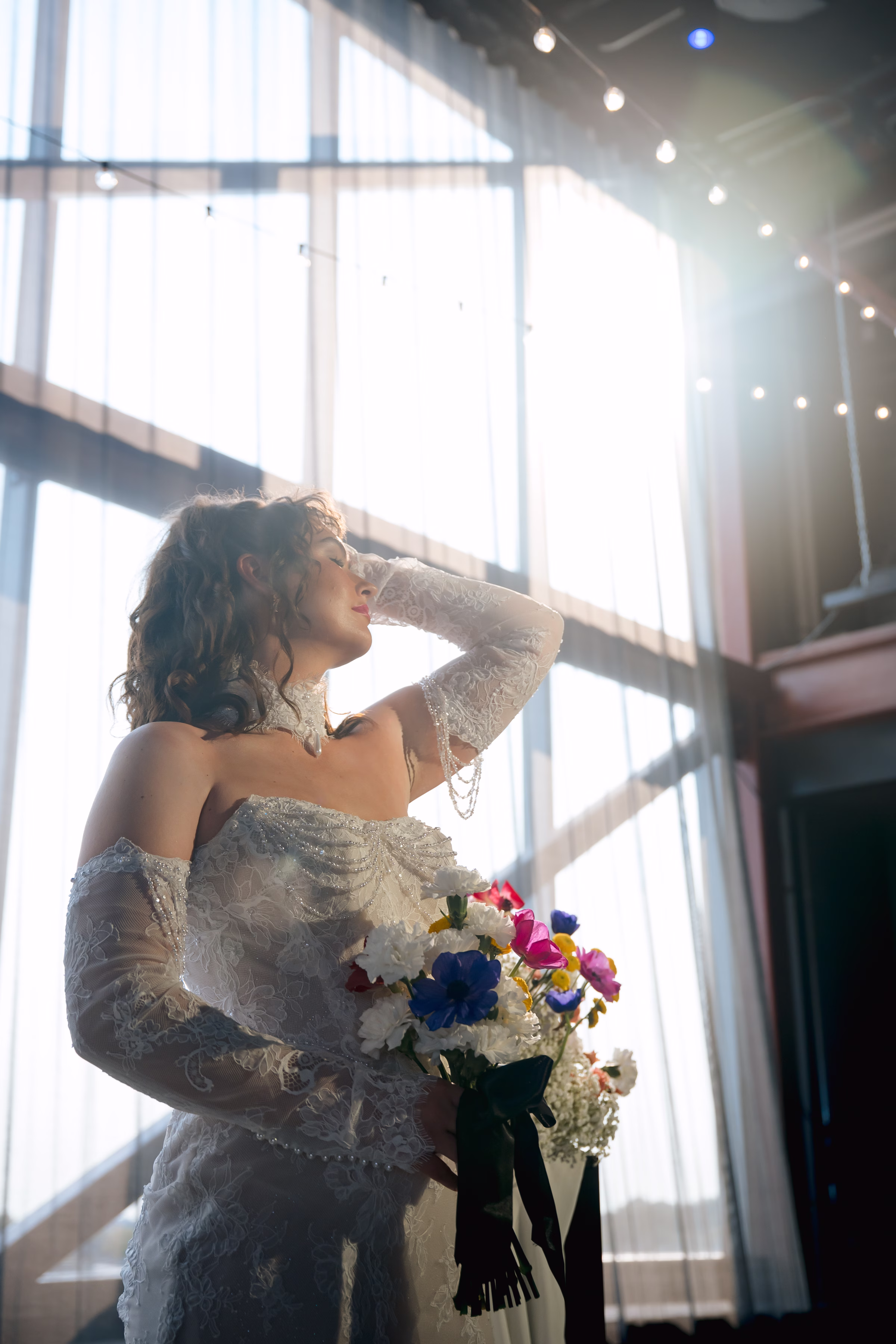 model Maggie poses in front of the floor-to-vaulted-ceiling windows at Jan Serr Studio holding a bouquet from Flowers for Dreams