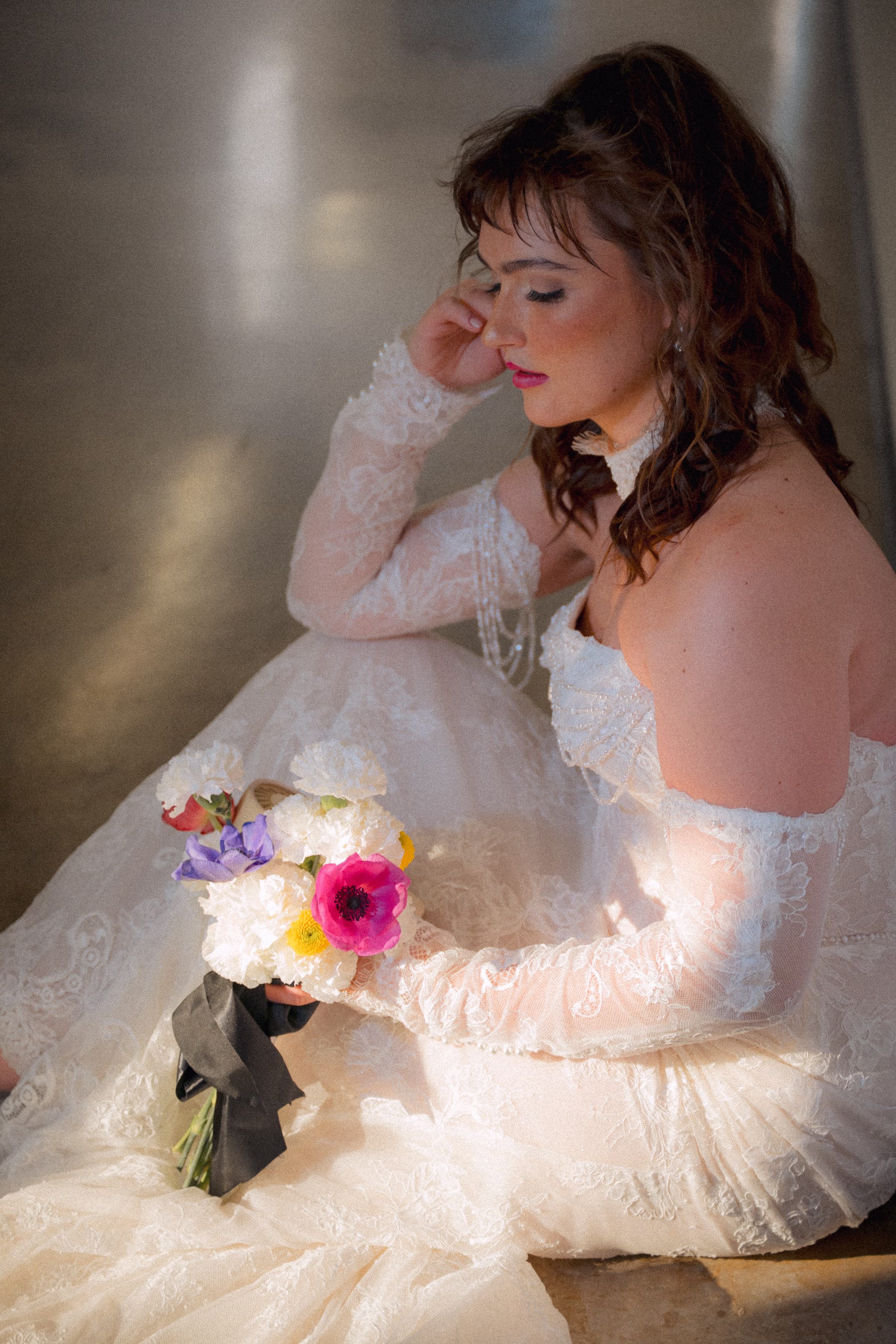 a bride model poses, seated, wearing a gown from Miss Ruby Bridal, with hair and makeup from Beauty Unveiled Agency