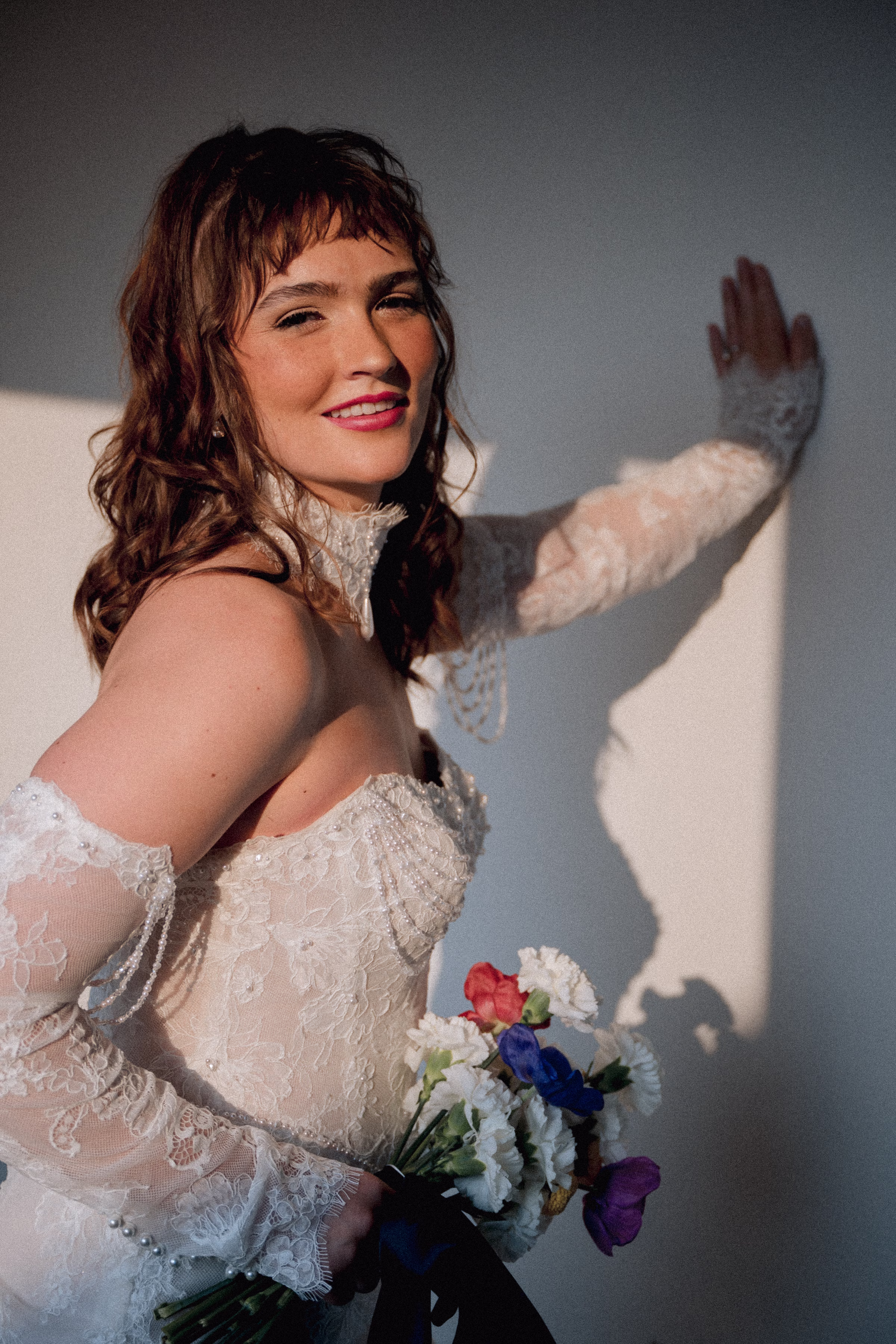 The Rock Agency bridal model, Maggie, poses with one hand against the wall, bouquet in her other hand