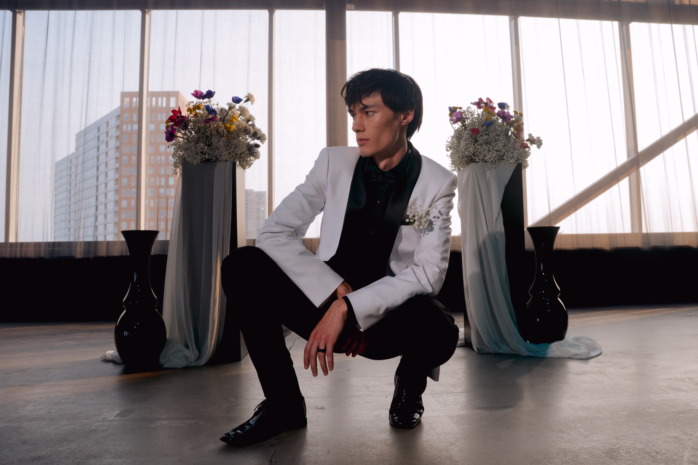 the groom model, David from The Rock Agency, crouches down at the ceremony space for Color Outside the Lines at Jan Serr Studio in Milwaukee, Wisconsin. He is wearing a white tuxedo jacket, black dress shirt, black pants, and black shoes from DuBois Formal Wear