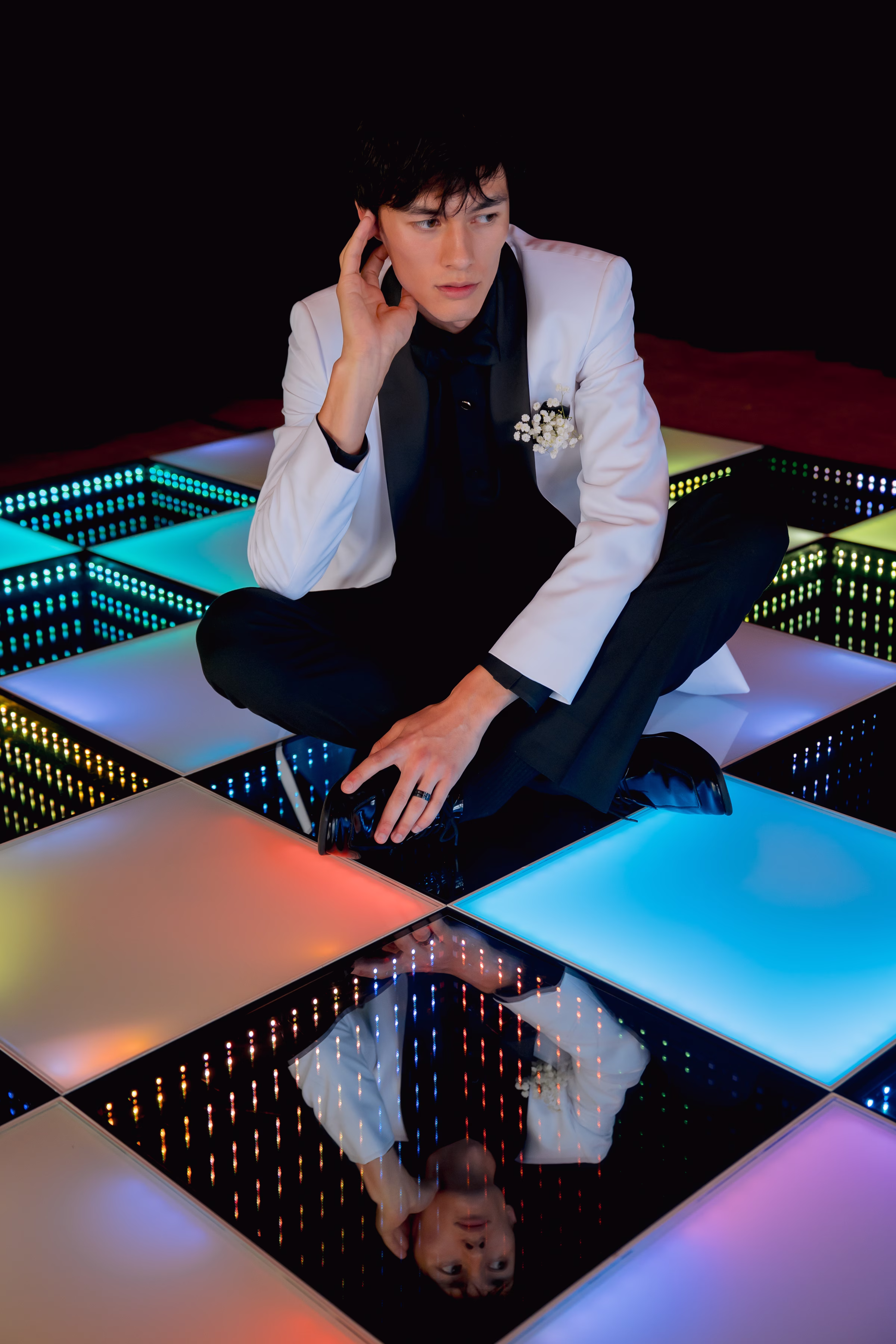 a groom sits on a colorful LED checkerboard dance floor