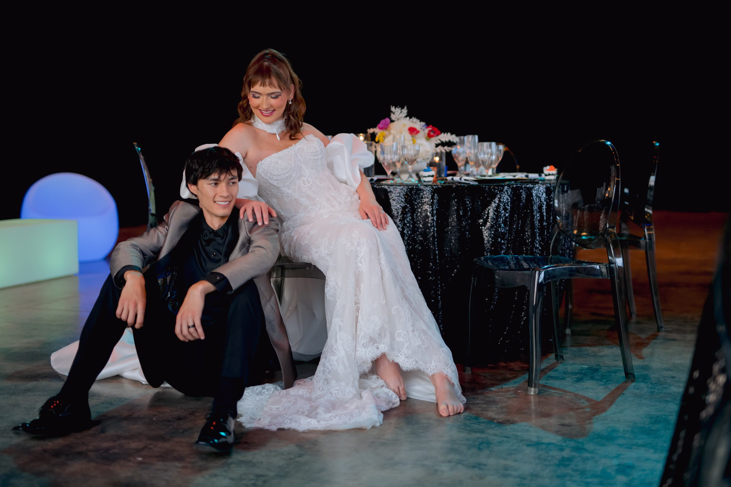 the bride and groom sit at the tablescape, with the groom seated on the floor and the pride leaning on him from her chair
