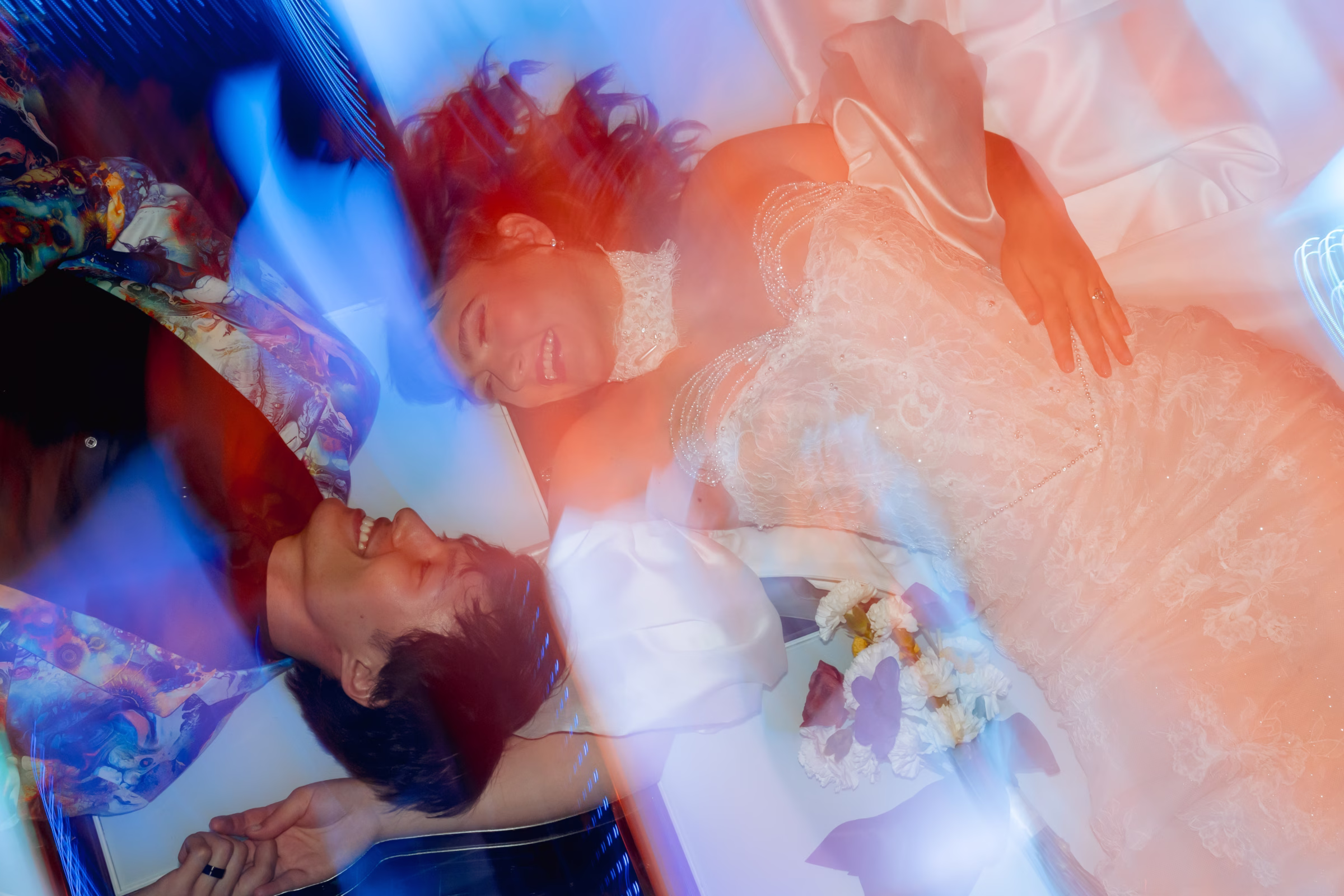 an overhead view of a bride and groom laying on a colorful LED dance floor. They are looking at one another as colors swirl around them
