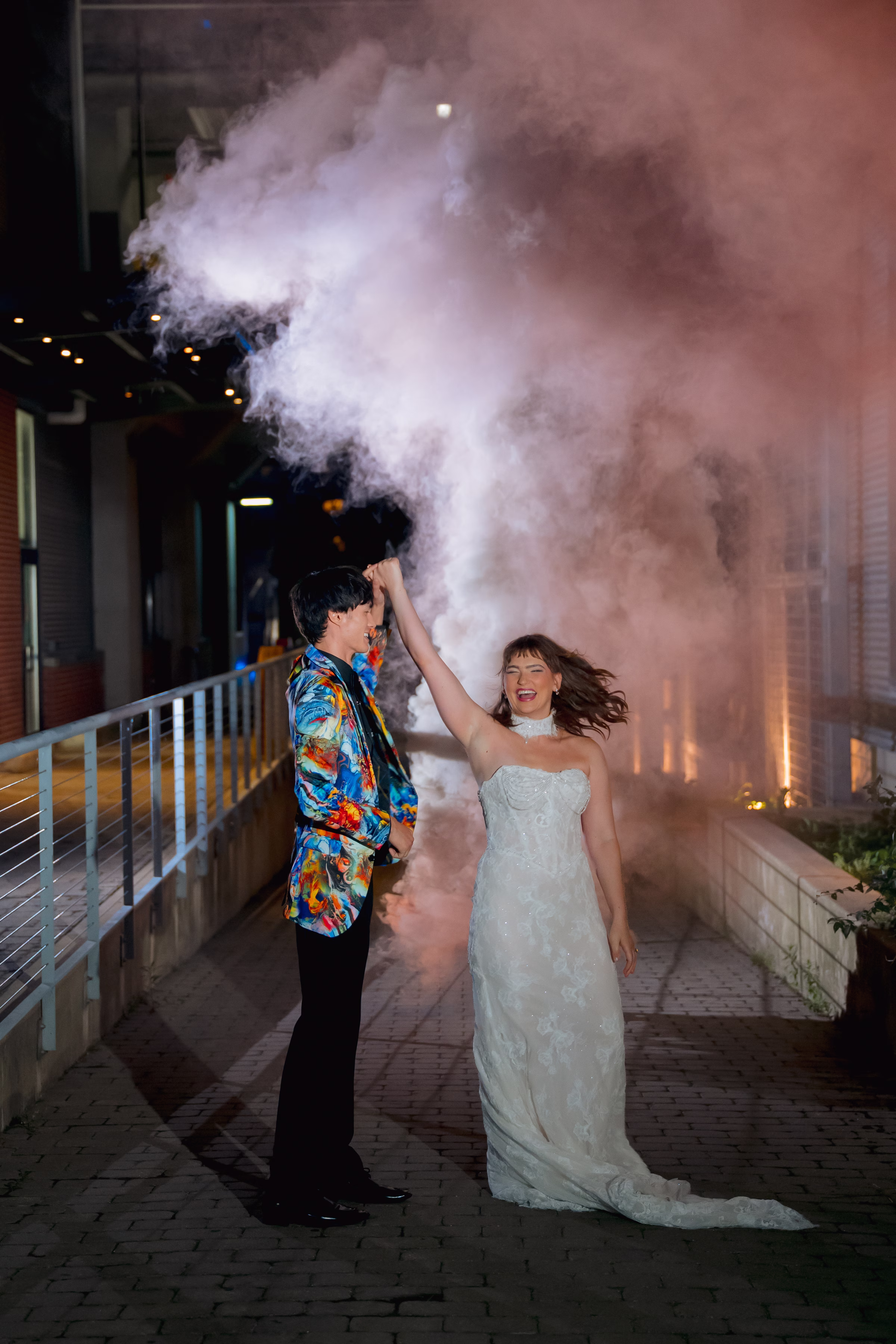 a groom twirls a bride as smoke bombs go off behind them in downtown Milwaukee