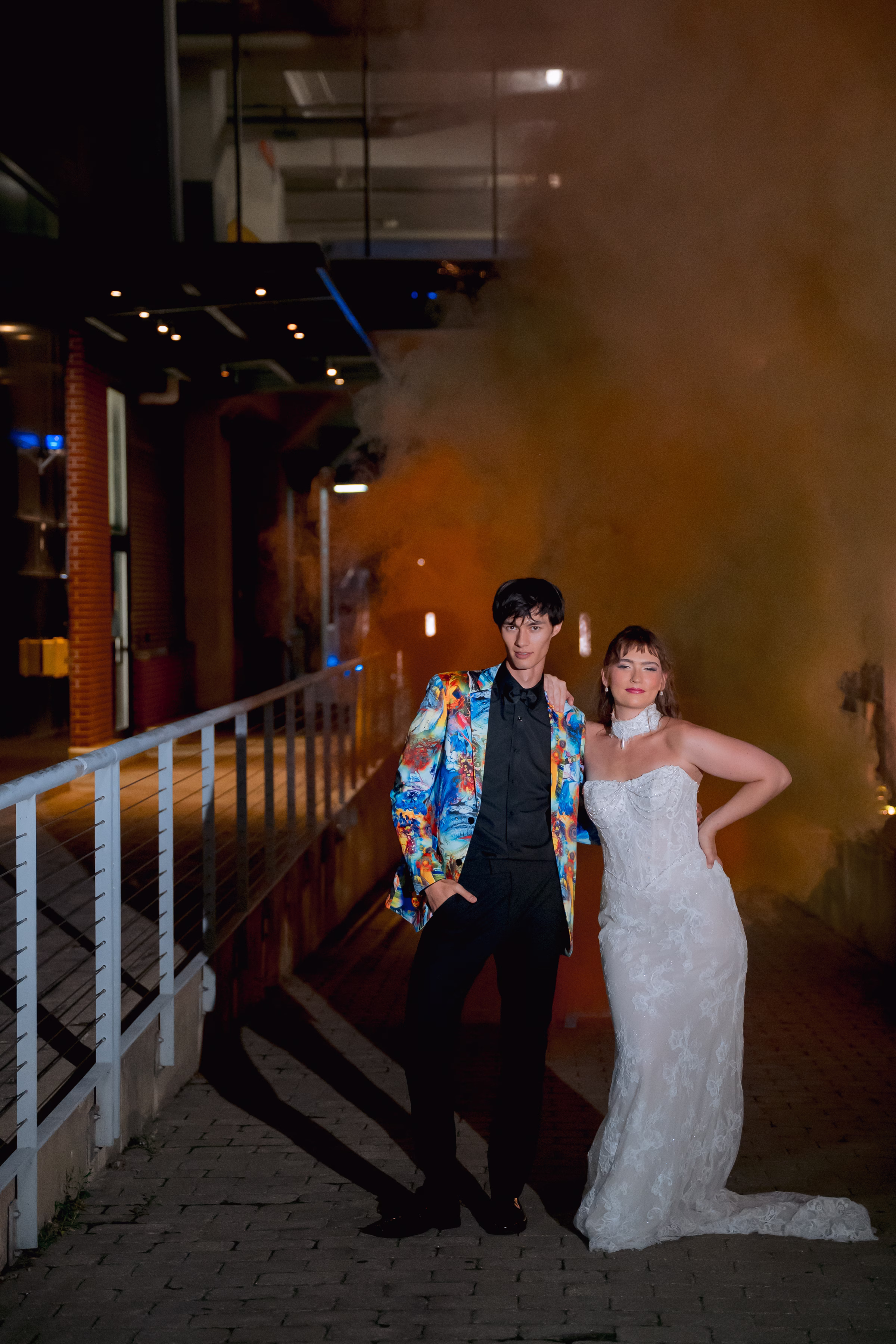 a bride and groom pose dramatically as smoke bombs go off behind them against a dark night sky