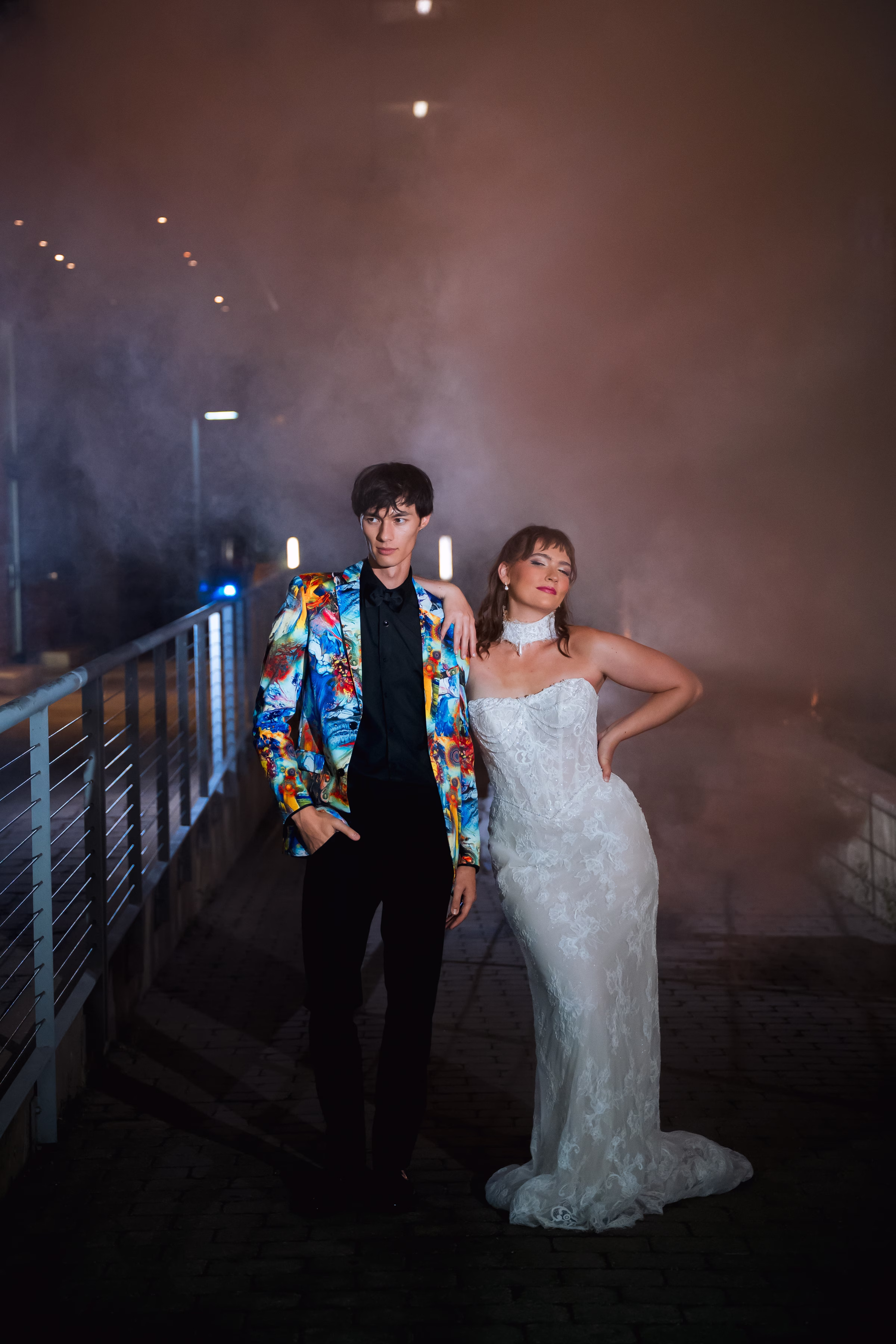 bride and groom models post side-by-side, looking away from the camera as smoke bombs go off behind them