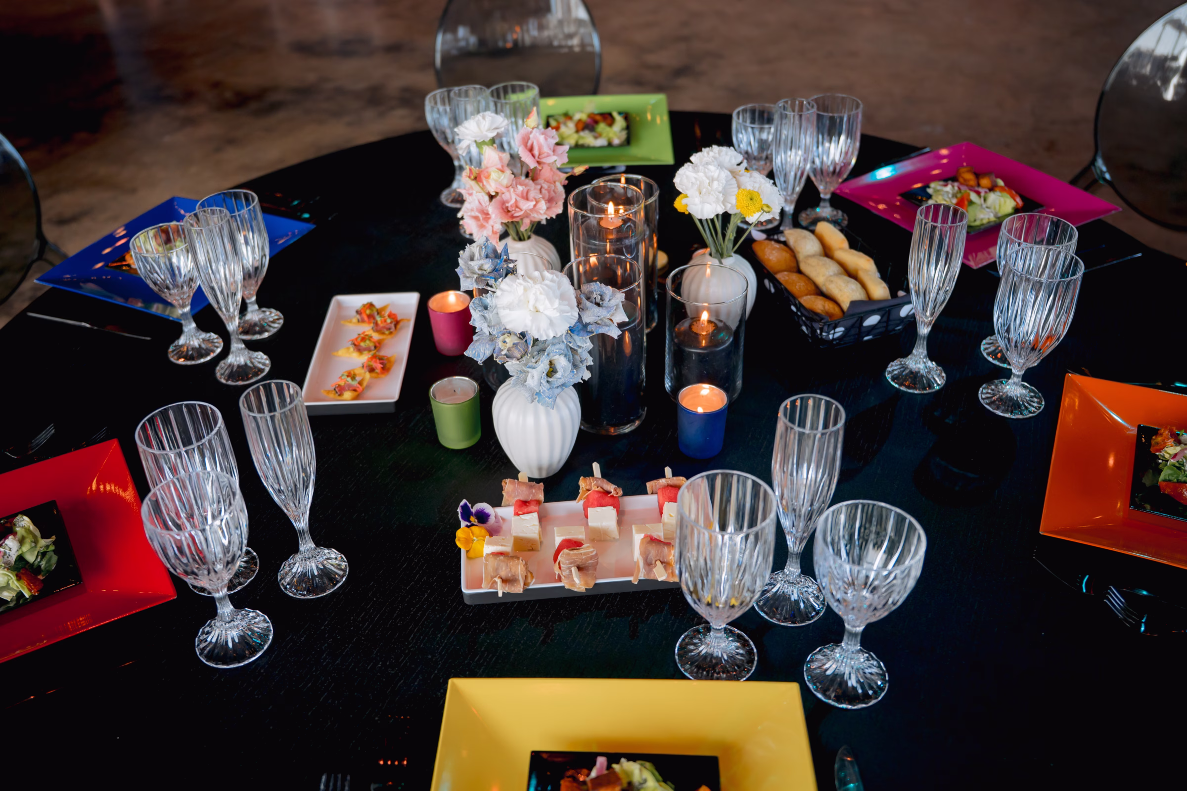 an overhead view of a wedding tablescape showing colorful square plates from Tablescape Event Rentals, floral centerpieces from Flowers for Dreams, and food and appetizers from Saz's Catering