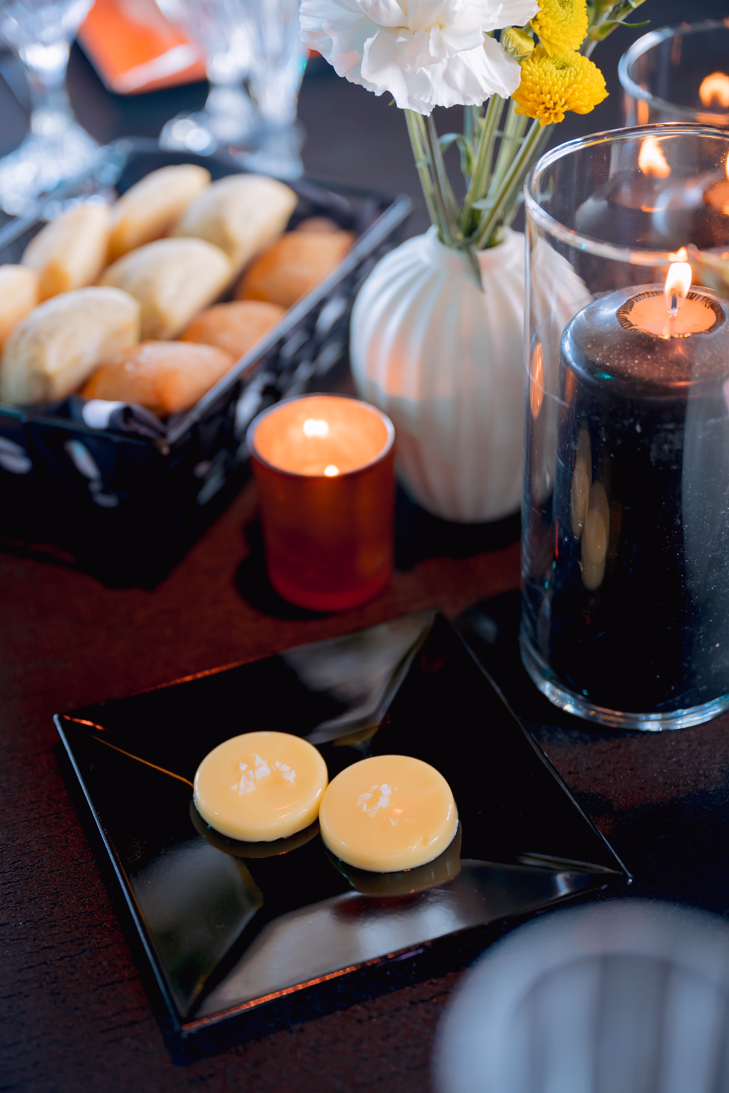 a close-up of the tablescape showing glowing candles, a vase, and dinner rolls & butter from Saz's Catering