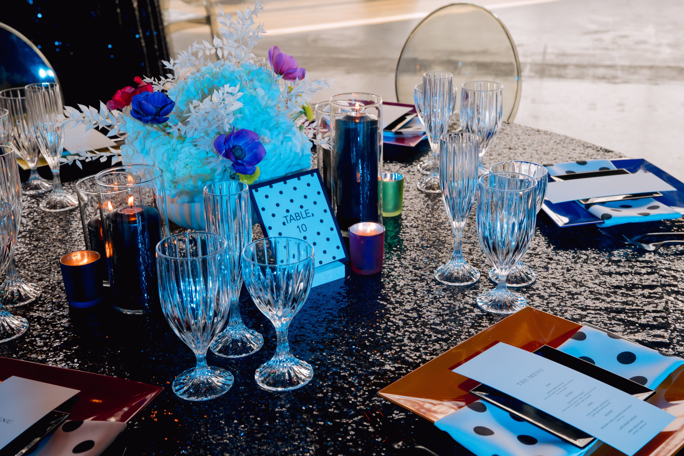 eclectic tablescape details on a black sequin tablecloth with clear acrylic chairs, crystal glassware, and colorful plating