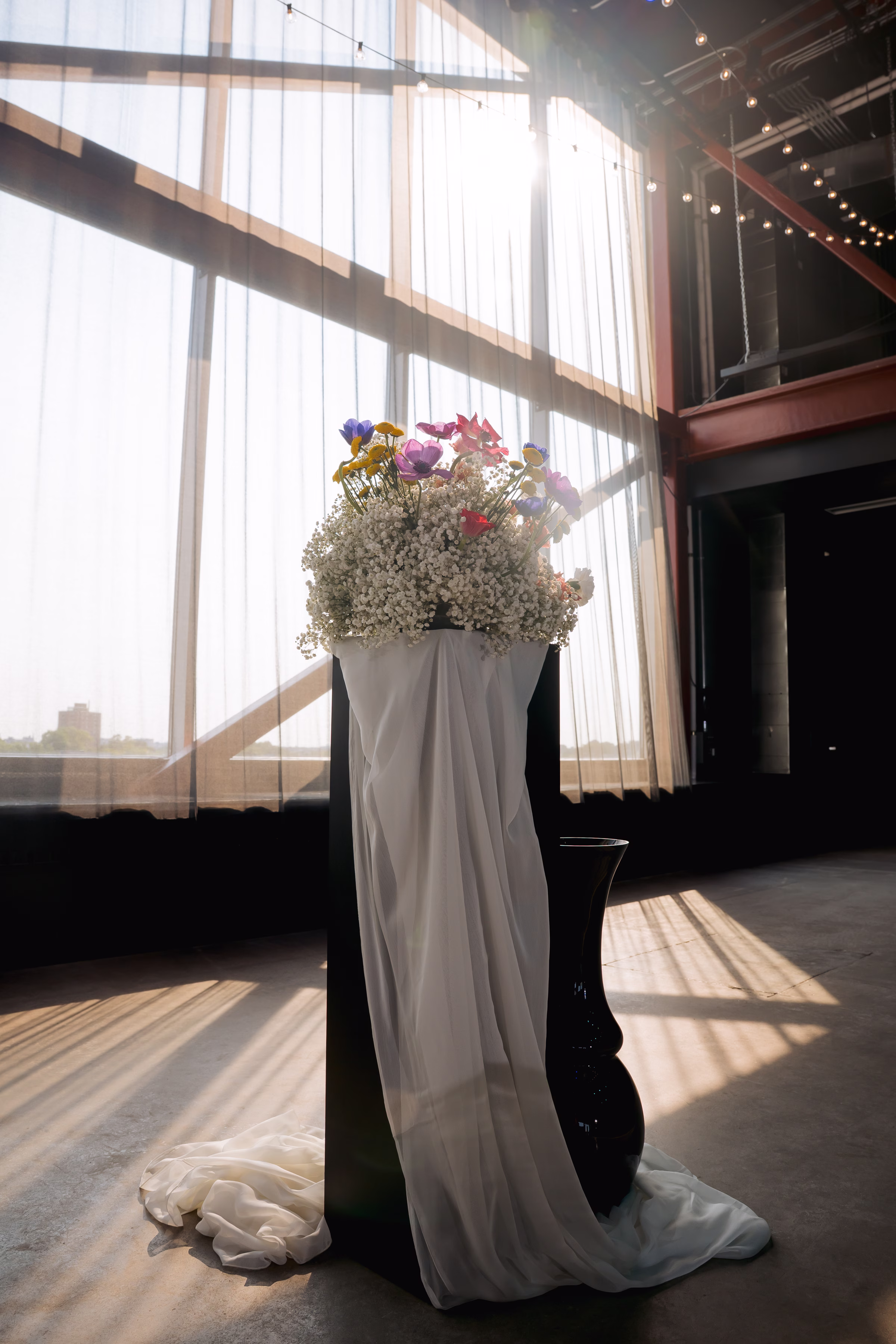 a detail shot of a decorative ceremony pillar draped in white cloth and topped with a floral arrangement from Flowers for Dreams