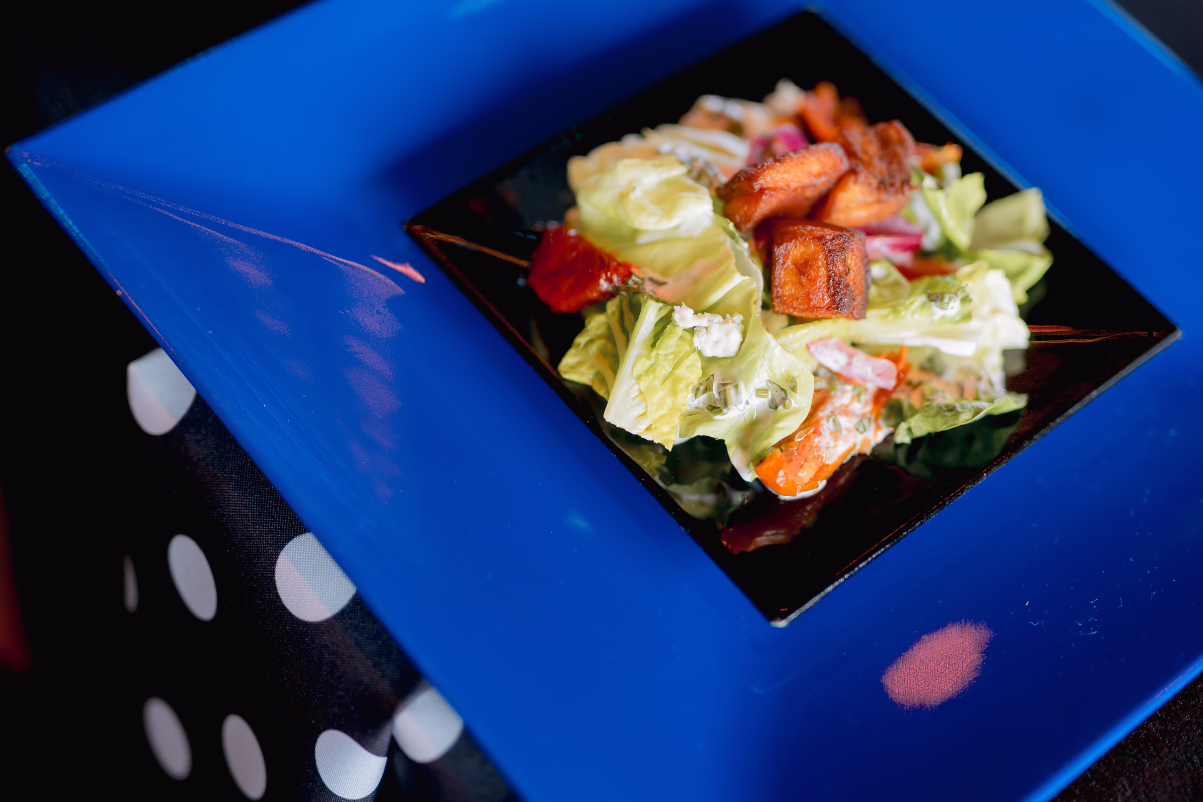 chopped salad from Saz's Catering served on layered black and blue square plating from Tablescape Event Rentals