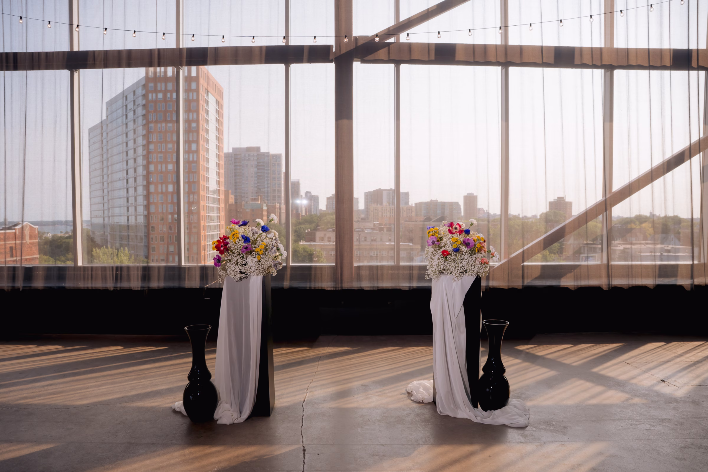 a ceremony backdrop featuring two pillars draped in cloth, florals from Flowers for Dreams, and dark vases
