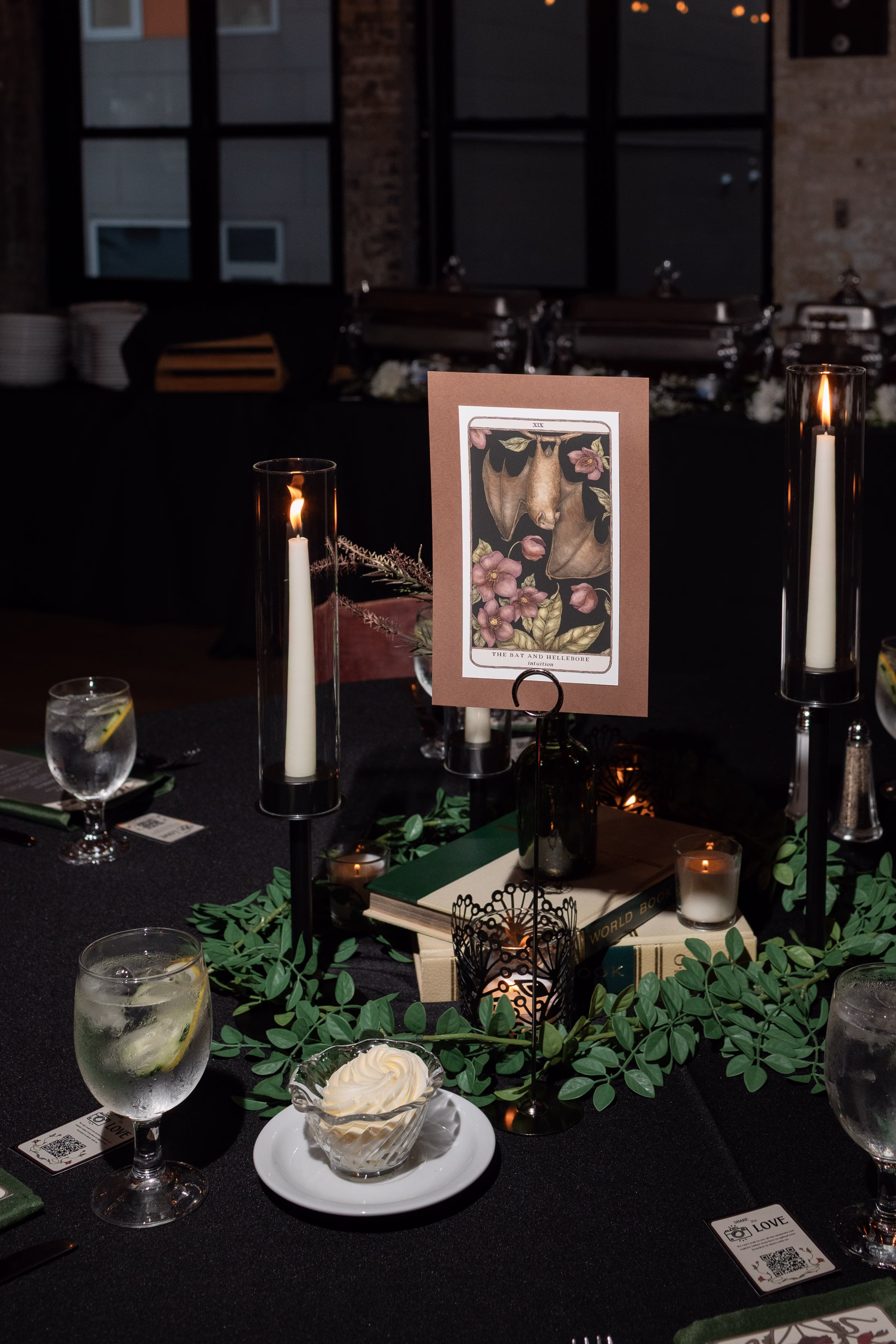 moody romantic fall wedding loft on broadway milwaukee reception centerpieces table numbers tarot 661 1043 - A Moody, Romantic Fall Wedding at The Loft on Broadway | Sarah + Nathan a custom tarot card table number surrounded by greenery, lit candles, and stacked on book centerpieces at a moody fall wedding reception in Milwaukee, Wisconsin