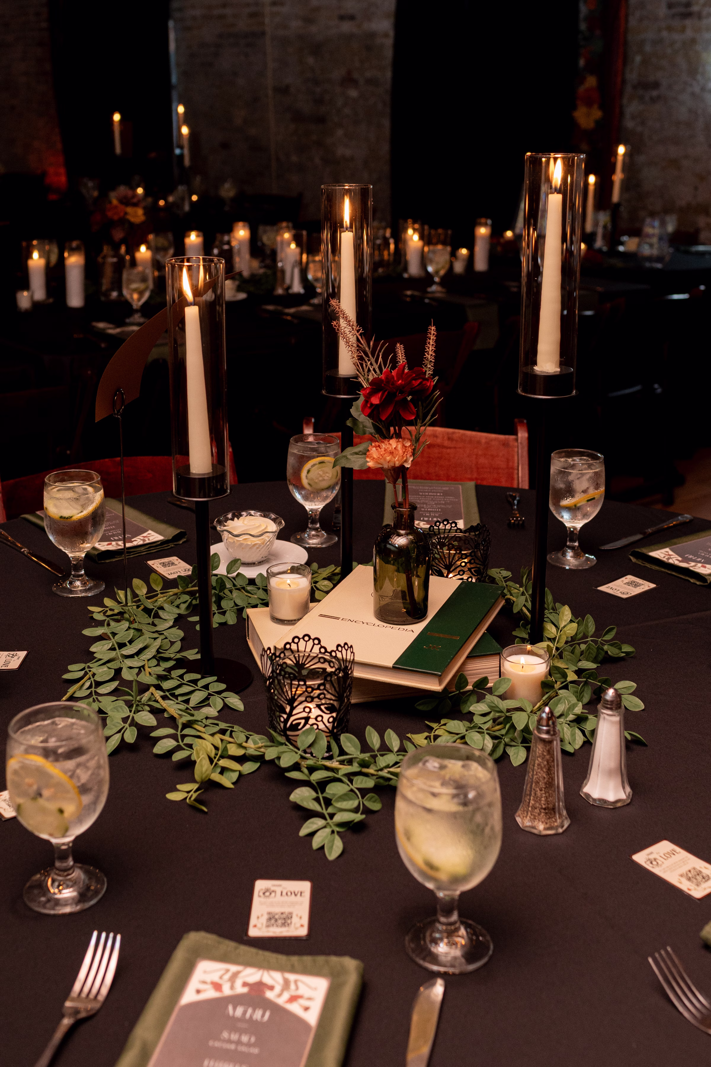 moody romantic fall wedding loft on broadway milwaukee reception centerpieces table numbers tarot 663 1052 - A Moody, Romantic Fall Wedding at The Loft on Broadway | Sarah + Nathan a detail photo showing a wedding centerpiece made from stacked books, bud vases of Sola Wood Flowers, candles, and greenery