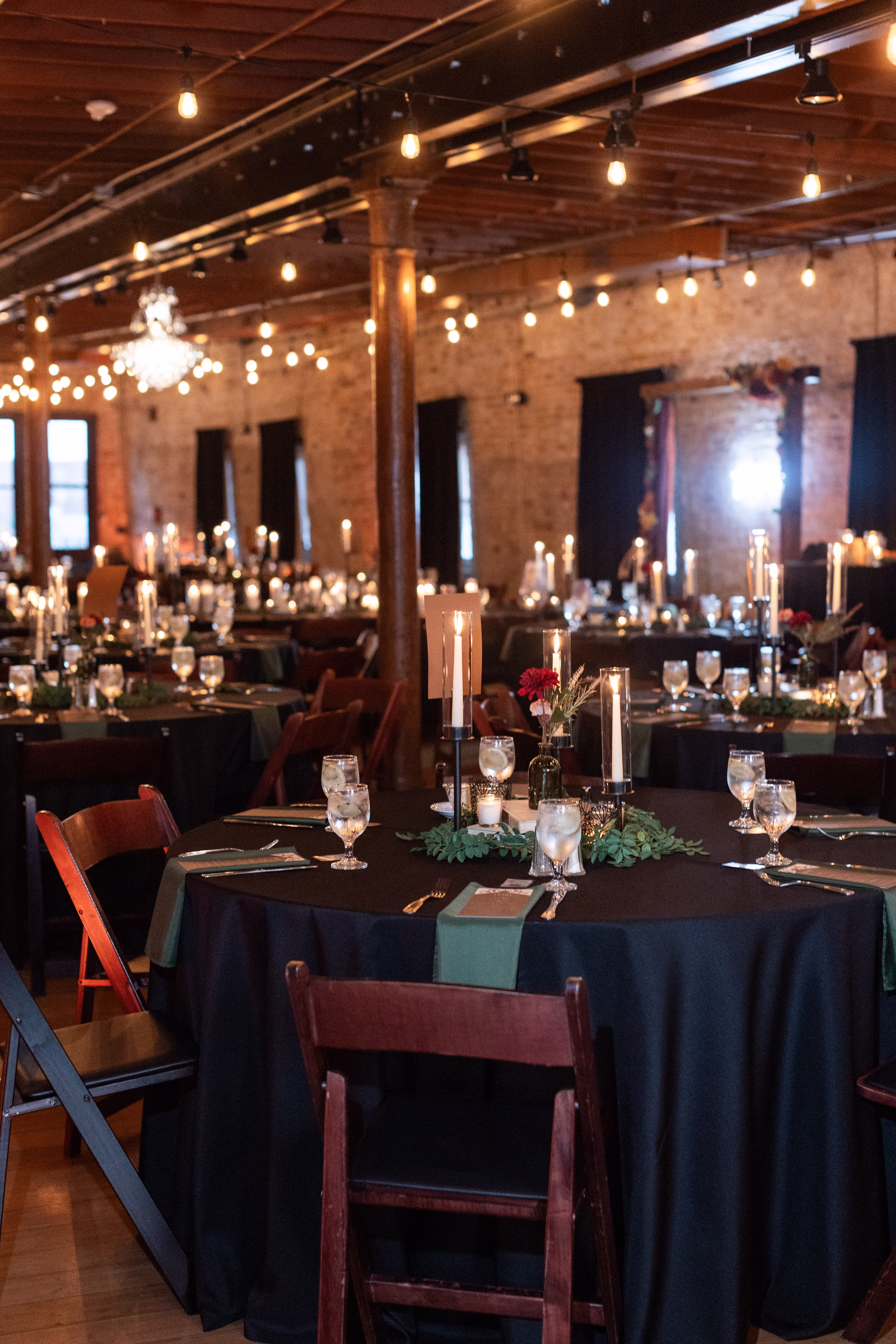 moody romantic fall wedding loft on broadway milwaukee reception details 656 1024 - A Moody, Romantic Fall Wedding at The Loft on Broadway | Sarah + Nathan wedding reception tables at a moody, romantic fall wedding at The Loft on Broadway in Milwaukee, Wisconsin. The tables all have glowing, lit candles, and there are string lights and chandeliers on the vaulted ceilings of the industrial-chic venue