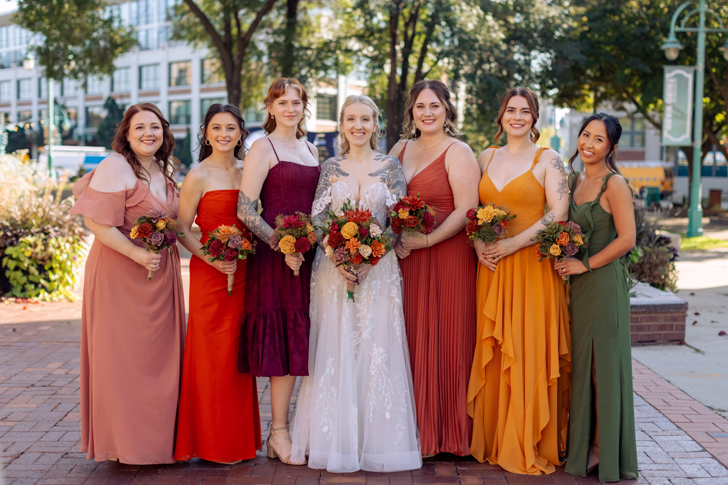 moody romantic fall wedding loft on broadway milwaukee wisconsin bridesmaids portraits 214 10443 - A Moody, Romantic Fall Wedding at The Loft on Broadway | Sarah + Nathan a bride stands with three bridesmaids on either side. The bridesmaids are all wearing uniquely colored fall dresses in green, orange, burnt orange, burgundy, red, and mauve