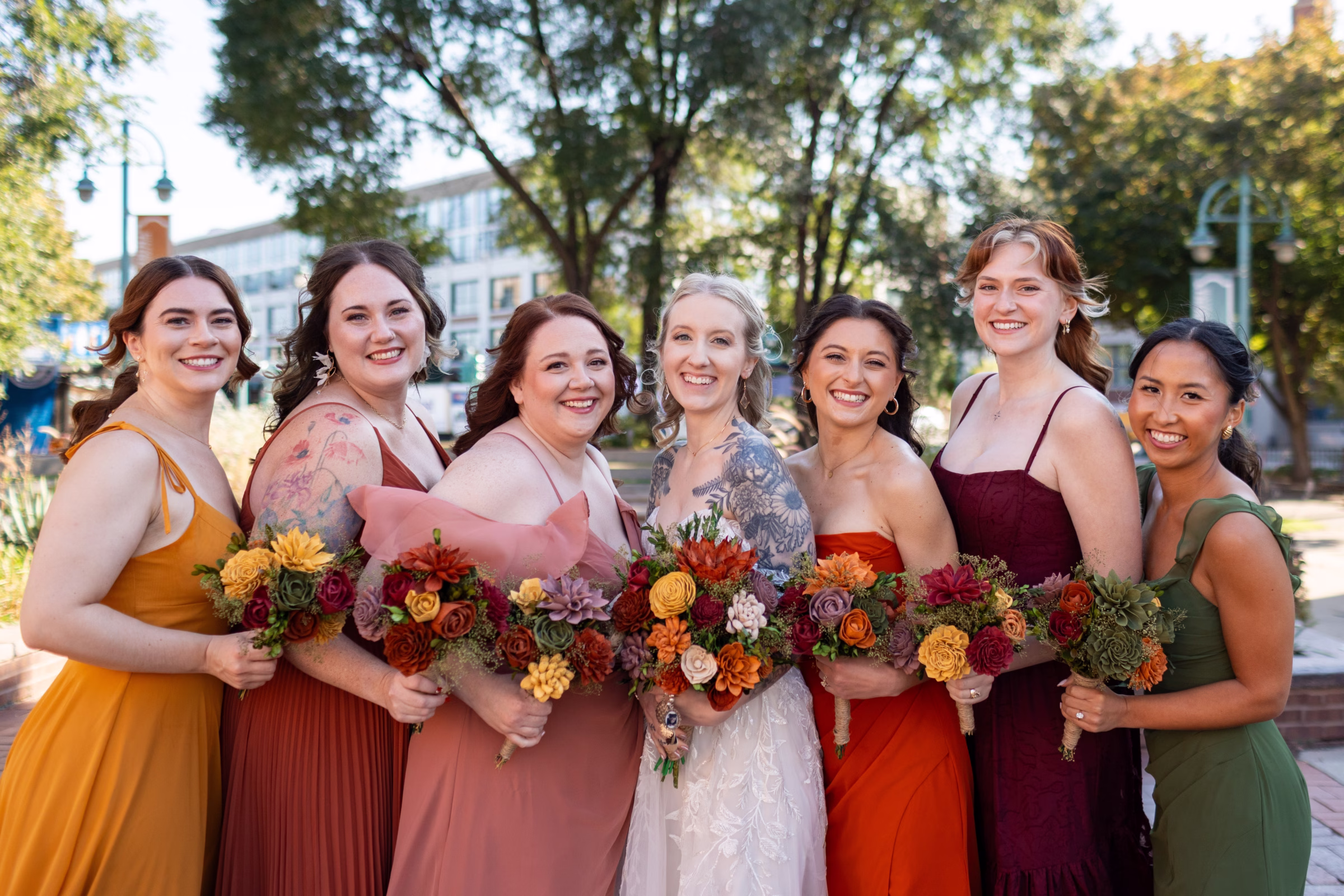moody romantic fall wedding loft on broadway milwaukee wisconsin bridesmaids portraits 244 0498 - A Moody, Romantic Fall Wedding at The Loft on Broadway | Sarah + Nathan a bride smiles alongside her bridesmaids, wearing a delicate lace dress from Strike Bridal Bar. Her bridesmaids are all wearing dresses in different styles and fall colors