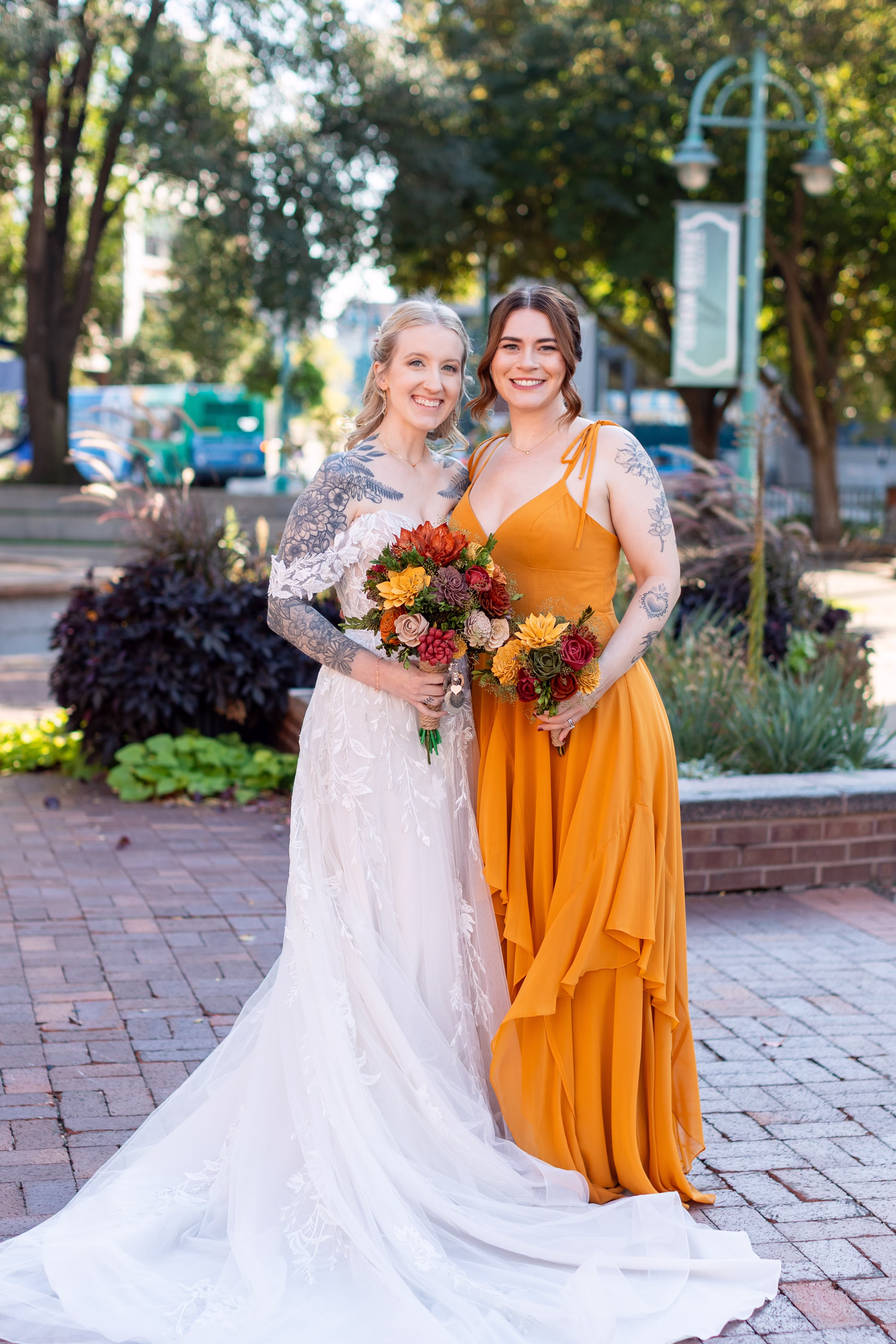 moody romantic fall wedding loft on broadway milwaukee wisconsin bridesmaids portraits 248 10464 - A Moody, Romantic Fall Wedding at The Loft on Broadway | Sarah + Nathan a bride poses with one of her bridesmaids. The bride is wearing a delicate lace dress from Strike Bridal Bar, and her bridesmaid is wearing a tangerine-colored, floor length dress with spaghetti straps and flowing layers in the skirt