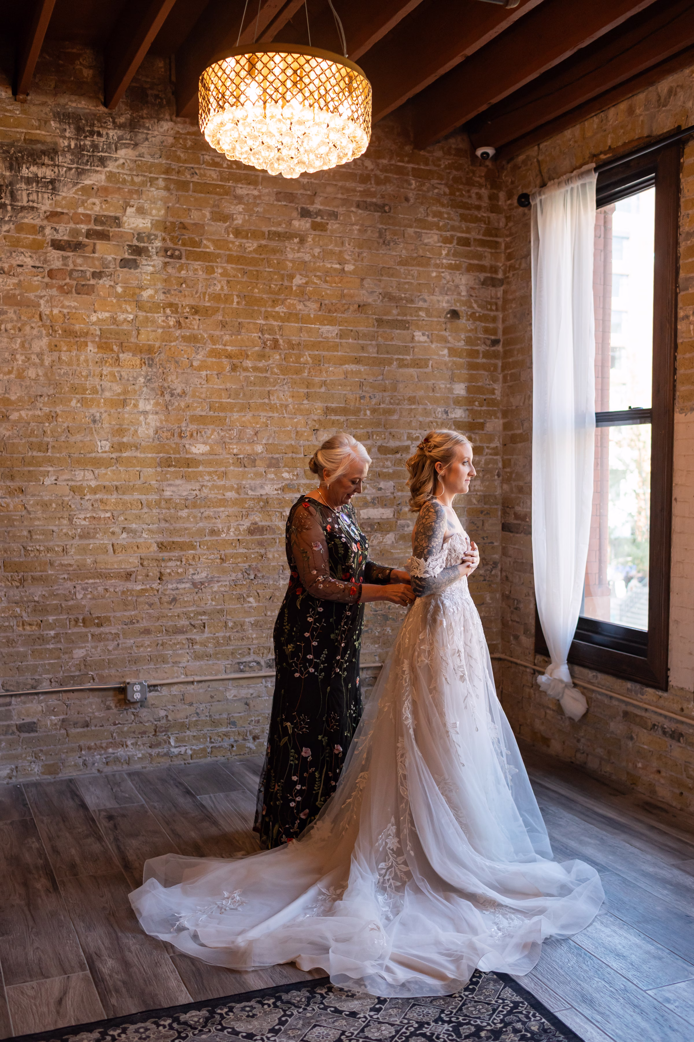moody romantic fall wedding loft on broadway milwaukee wisconsin getting ready 128 0169 - A Moody, Romantic Fall Wedding at The Loft on Broadway | Sarah + Nathan a family member helps a bride into her wedding dress at The Loft on Broadway