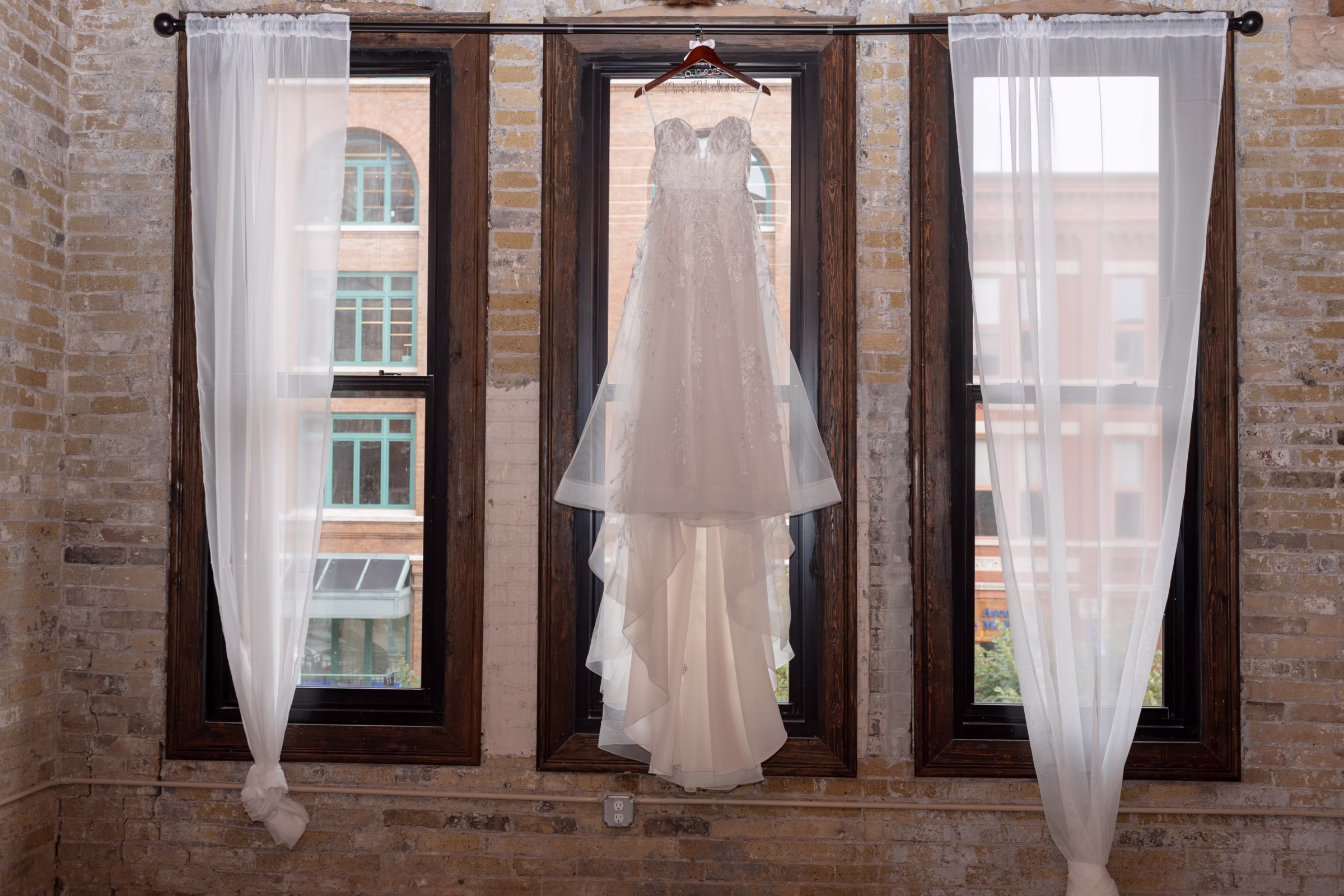 moody romantic fall wedding loft on broadway milwaukee wisconsin getting ready 3 0010 - A Moody, Romantic Fall Wedding at The Loft on Broadway | Sarah + Nathan a wedding dress from Strike Bridal Bar hangs from a window at The Loft on Broadway in Milwaukee, Wisconsin