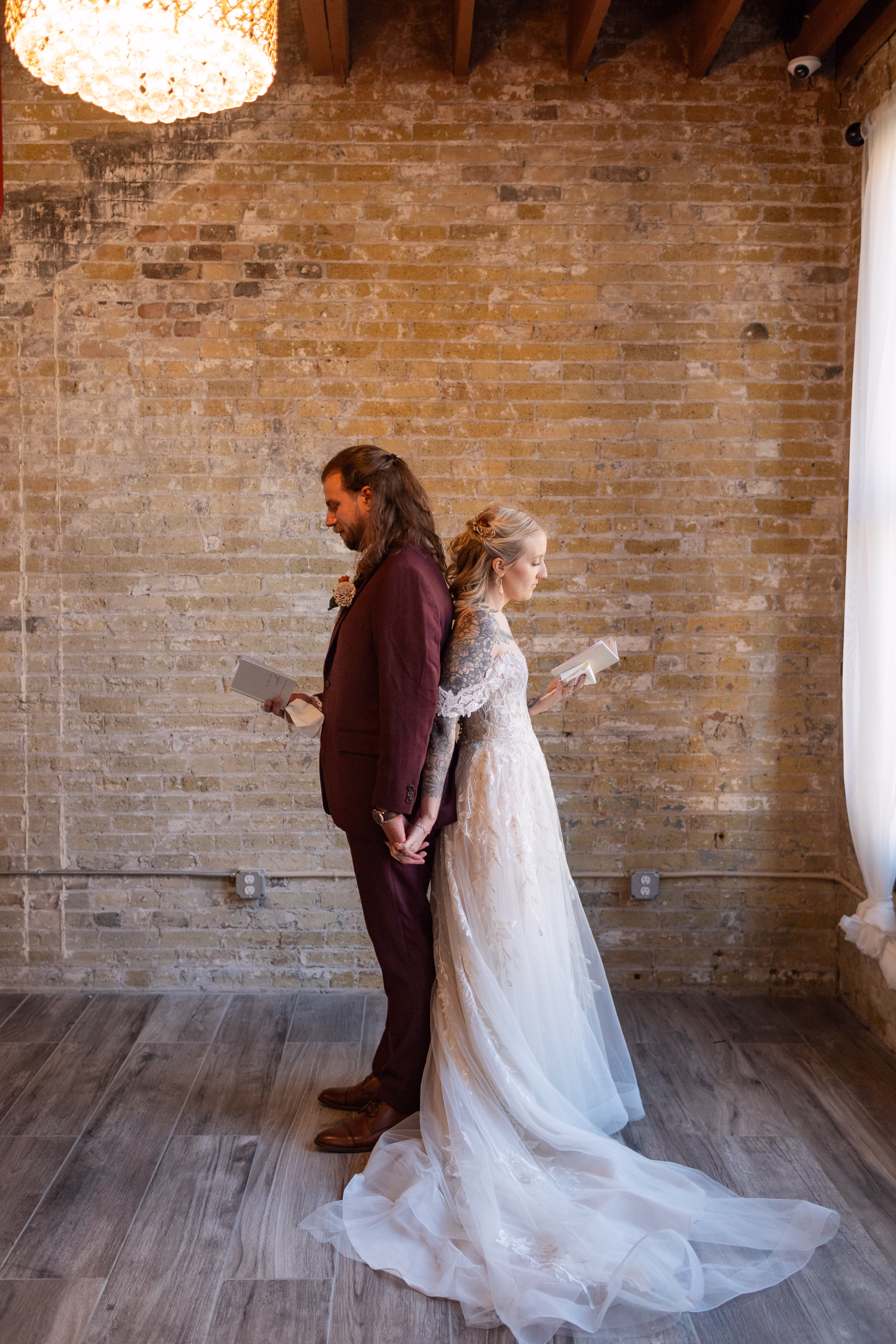 moody romantic fall wedding loft on broadway milwaukee wisconsin getting ready 304 0517 - A Moody, Romantic Fall Wedding at The Loft on Broadway | Sarah + Nathan a bride and groom stand back-to-back, holding hands while reading private vows at The Loft on Broadway in Milwaukee, Wisconsin