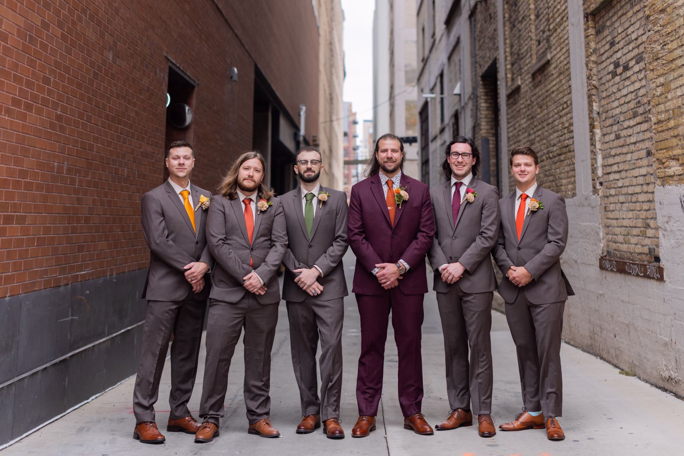 moody romantic fall wedding loft on broadway milwaukee wisconsin groomsmen 52 10102 - A Moody, Romantic Fall Wedding at The Loft on Broadway | Sarah + Nathan a groom and his groomsman stand in an alley with brick walls on either side in Milwaukee, Wisconsin. They are wearing suits from Studio Suits