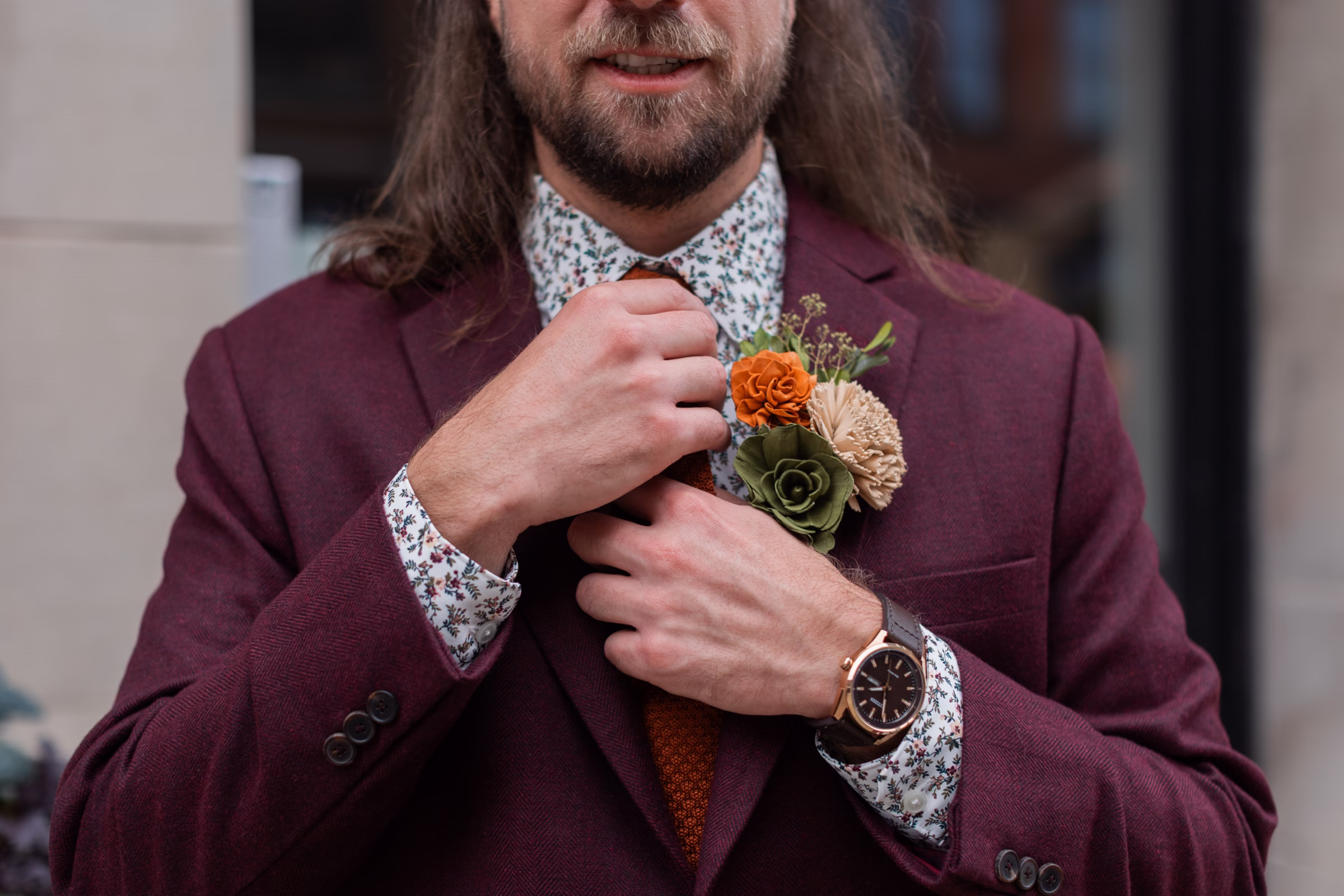 moody romantic fall wedding loft on broadway milwaukee wisconsin groomsmen 77 10206 - A Moody, Romantic Fall Wedding at The Loft on Broadway | Sarah + Nathan a close-up on a groom, showing his burgundy suit jacket, floral-patterned dress shirt, burnt orange tie, wood flower boutonnière, and watch