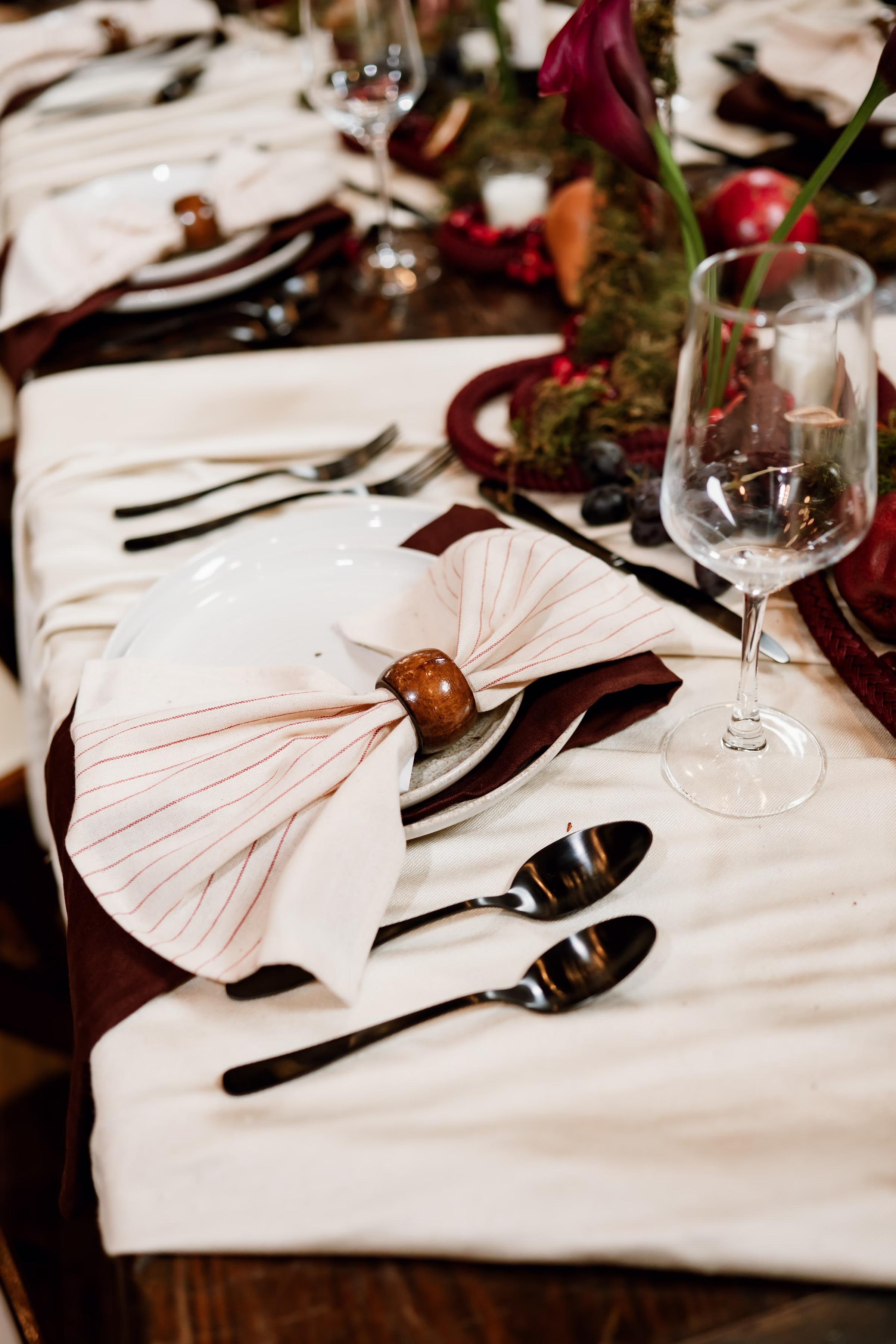CorrinaNicolePhotography AmandaJenPhotography MercantileHall StyledShoot 112825 6 - Rich Velvet Fall Wedding Inspiration at Mercantile Hall in Burlington, Wisconsin a detail photo showing a place setting that includes a white and burgundy striped napkin with a wooden napkin ring