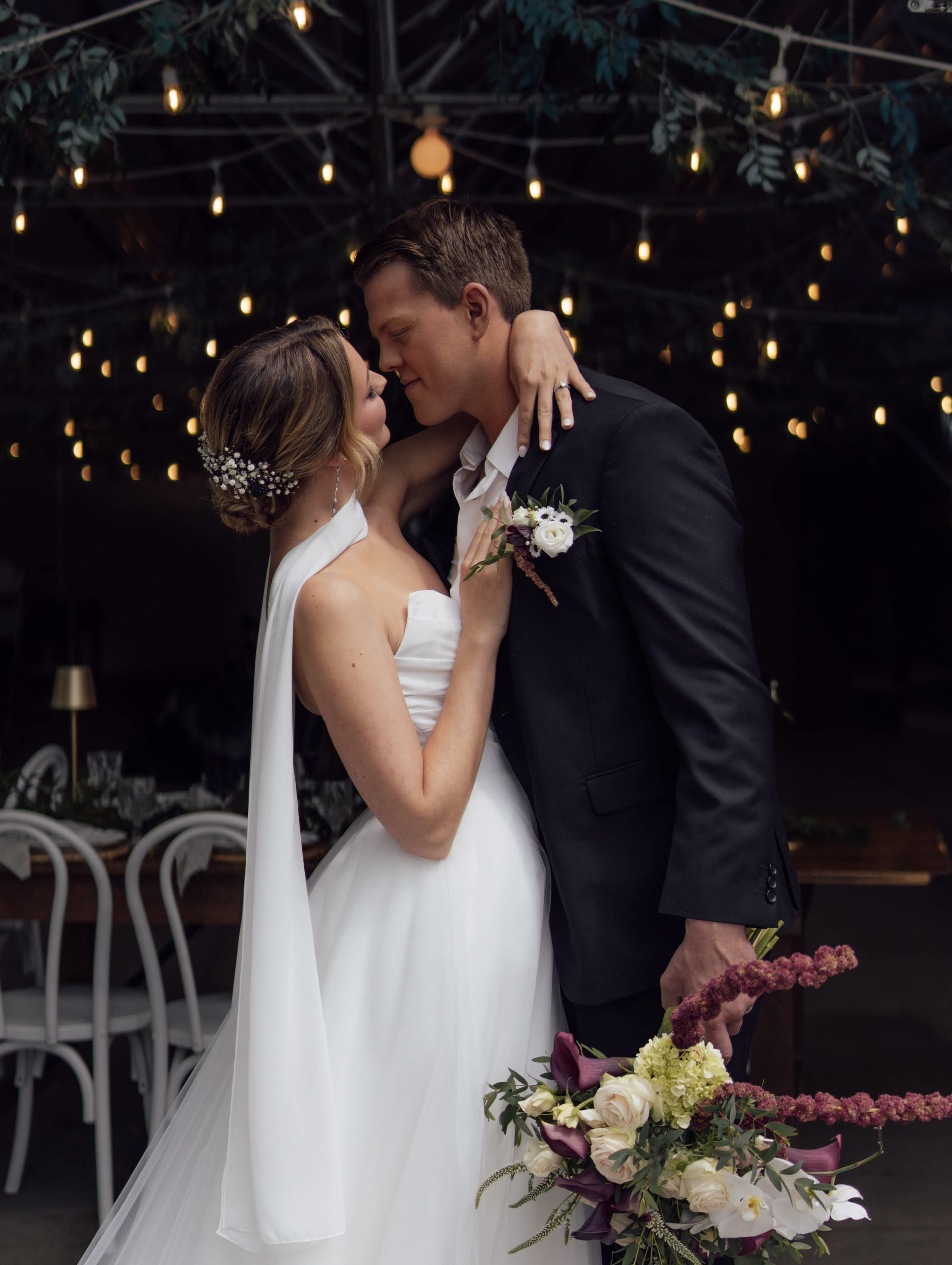 An intimate evening wedding reception coordinated by Northwoods Event Services, featuring a close embrace between the bride and groom under glowing cafe string lights and lush ceiling greenery.
