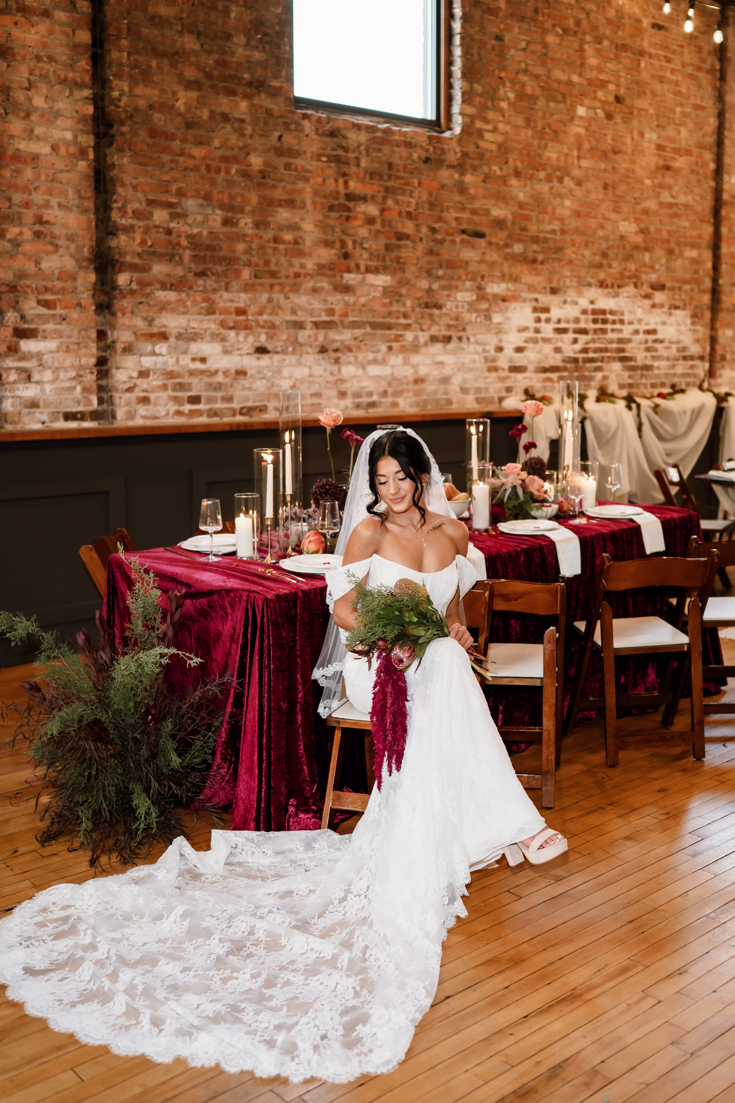 rich velvet fall wedding inspiration mercantile hall burlington wisconsin burgundy tablescape bride fashion 224 - Rich Velvet Fall Wedding Inspiration at Mercantile Hall in Burlington, Wisconsin a bride is seated at a fall tablescape with burgundy velvet tablecloth. She is wearing a gown from Bon Bon Belle Bridal Boutique, with a cathedral-length lace train