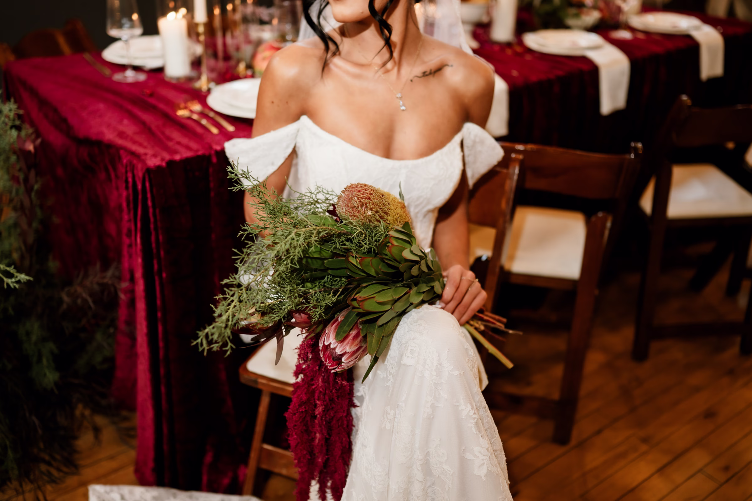 rich velvet fall wedding inspiration mercantile hall burlington wisconsin burgundy tablescape bride fashion 228 - Rich Velvet Fall Wedding Inspiration at Mercantile Hall in Burlington, Wisconsin a bride is seated at a fall tablescape with burgundy velvet tablecloth. She is holding a bouquet made of rust-colored banksia, blush protea, cascading burgundy amaranthus, and sculptural leucadendron accented with delicate, airy greenery