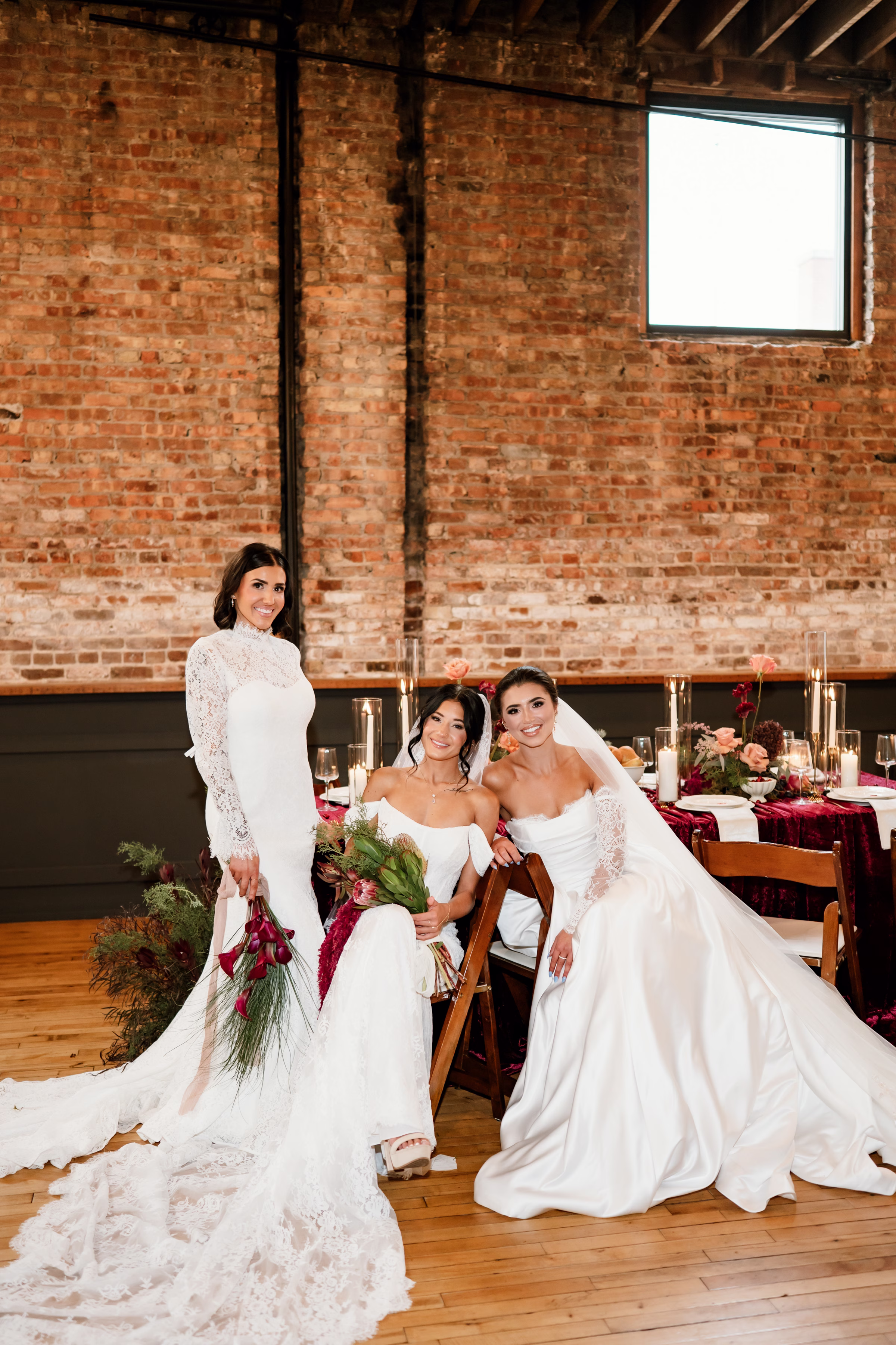 rich velvet fall wedding inspiration mercantile hall burlington wisconsin burgundy tablescape bride fashion 230 - Rich Velvet Fall Wedding Inspiration at Mercantile Hall in Burlington, Wisconsin three brides pose at a rich velvet tablescape at Mercantile Hall in Burlington, Wisconsin. They are each wearing a distinct dress from Bon Bon Belle Bridal Boutique, and two brides are holding bouquets from The Flower Bar and Anna's Florals