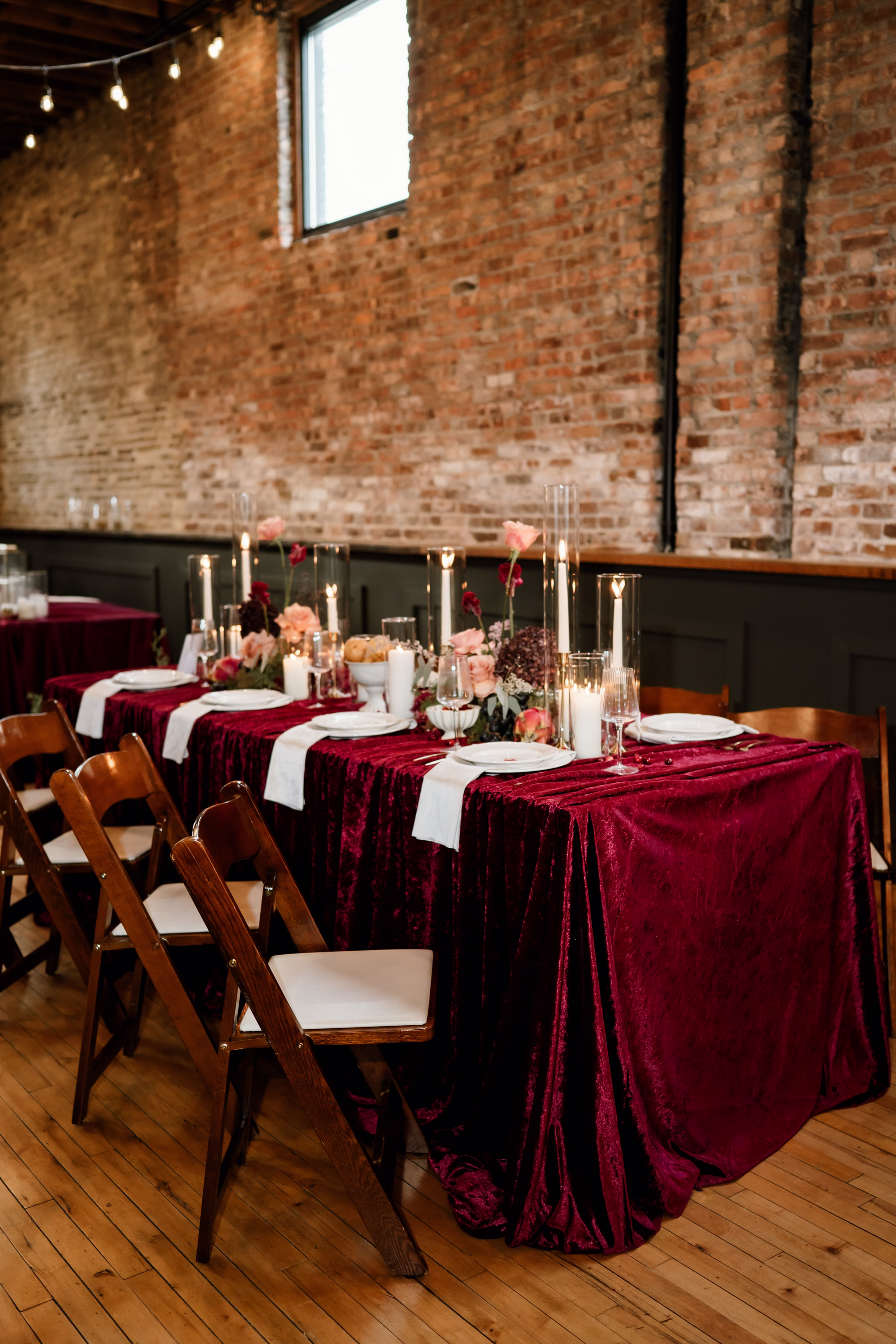 rich velvet fall wedding inspiration mercantile hall burlington wisconsin burgundy tablescape details 194 - Rich Velvet Fall Wedding Inspiration at Mercantile Hall in Burlington, Wisconsin a rich velvet fall wedding tablescape at Mercantile Hall, showing a table layered with a burgundy velvet tablecloth, white plating, white satin napkins, gold flatware, crystal glassware, candles, floral centerpieces, and fruit as décor