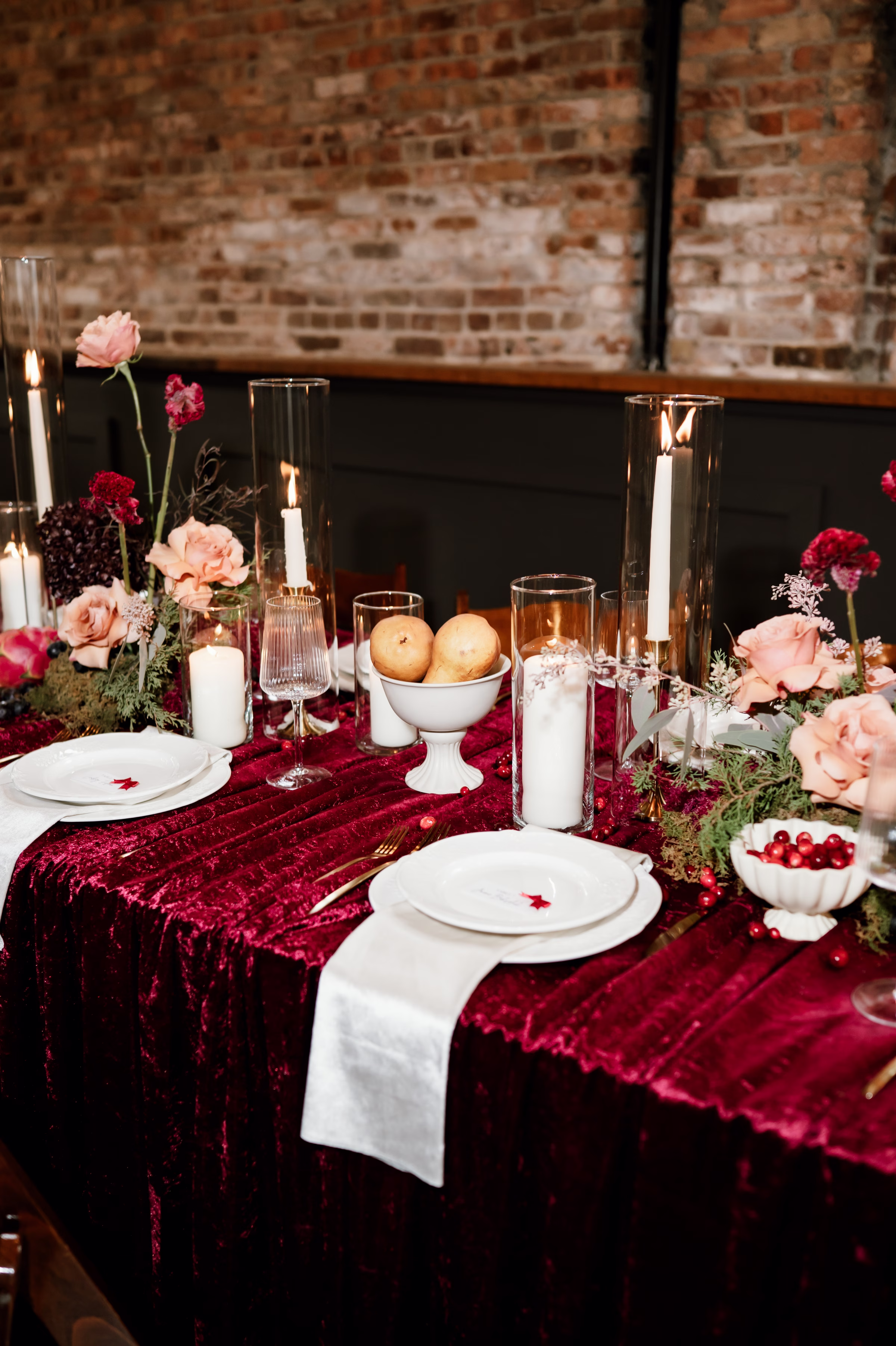 rich velvet fall wedding inspiration mercantile hall burlington wisconsin burgundy tablescape details 196 - Rich Velvet Fall Wedding Inspiration at Mercantile Hall in Burlington, Wisconsin an angled photo of a fall wedding tablescape with burgundy velvet tablecloth, white plating and napkins, candles, crystal glassware, and fruit as décor