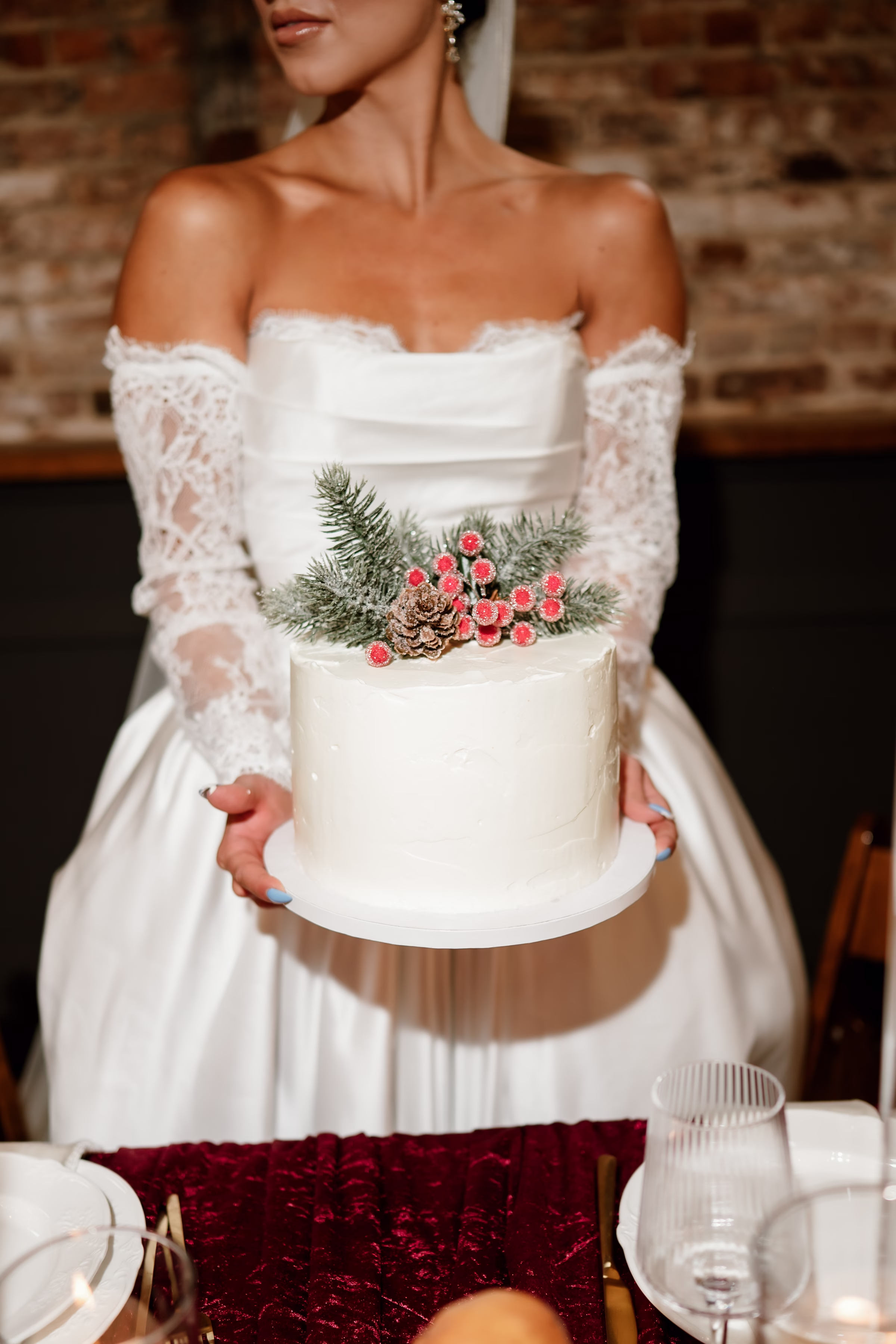 rich velvet fall wedding inspiration mercantile hall burlington wisconsin cake fruit tablescape 238 - Rich Velvet Fall Wedding Inspiration at Mercantile Hall in Burlington, Wisconsin a bride holds out a single-layer wedding cake by Kindred Bakeshop topped with seasonal pine branches, a pine cone, and winter berries
