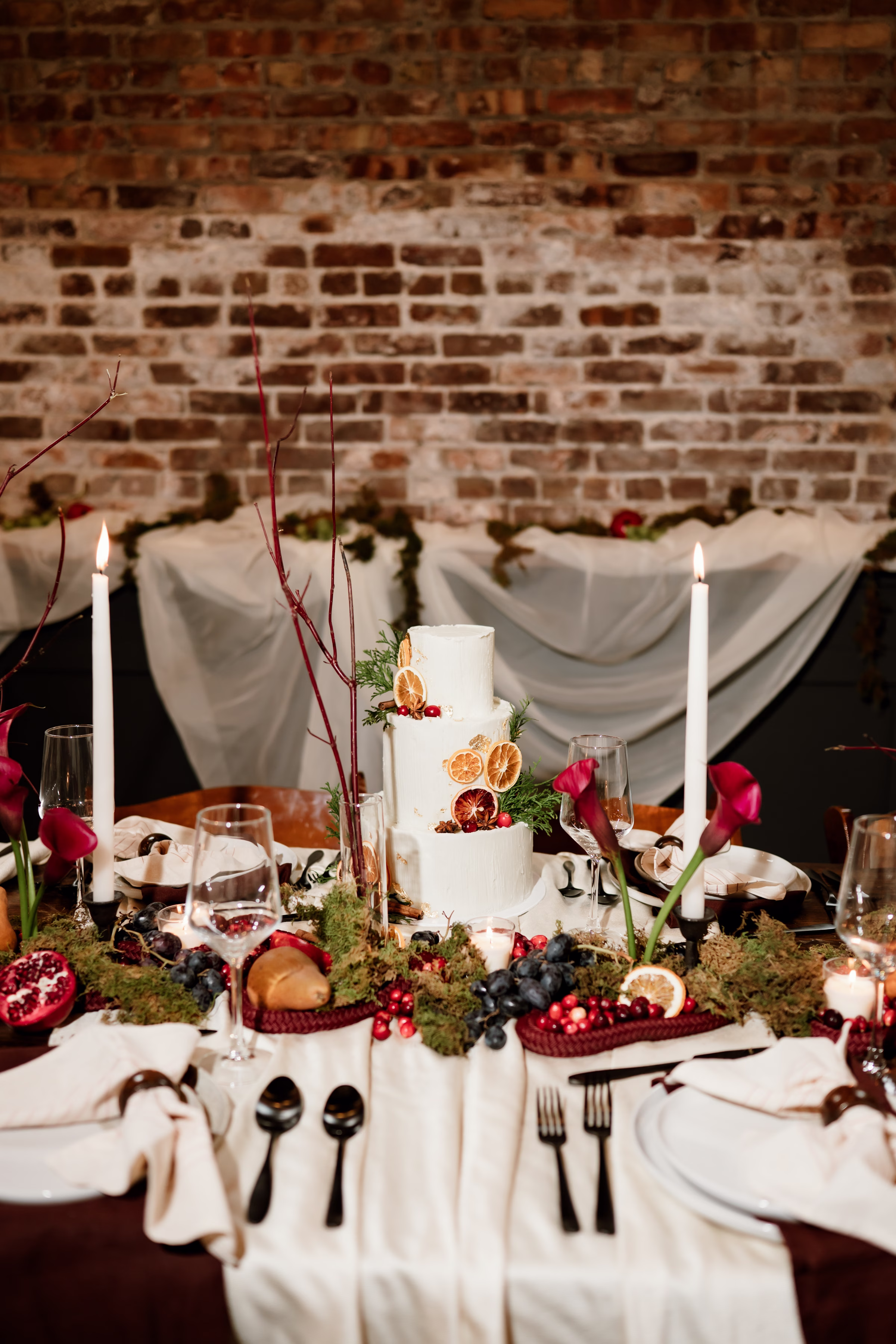 rich velvet fall wedding inspiration mercantile hall burlington wisconsin cake fruit tablescape 40 - Rich Velvet Fall Wedding Inspiration at Mercantile Hall in Burlington, Wisconsin a three-layer white wedding cake by Kindred Bakeshop, decorated with orange slices, grapefruit slices, and cranberries, and surrounded by mossy foliage and fruit as décor